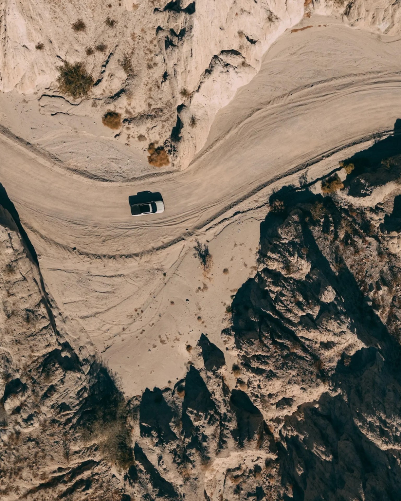 White pickup truck driving on a winding dirt road through a rocky, arid landscape.