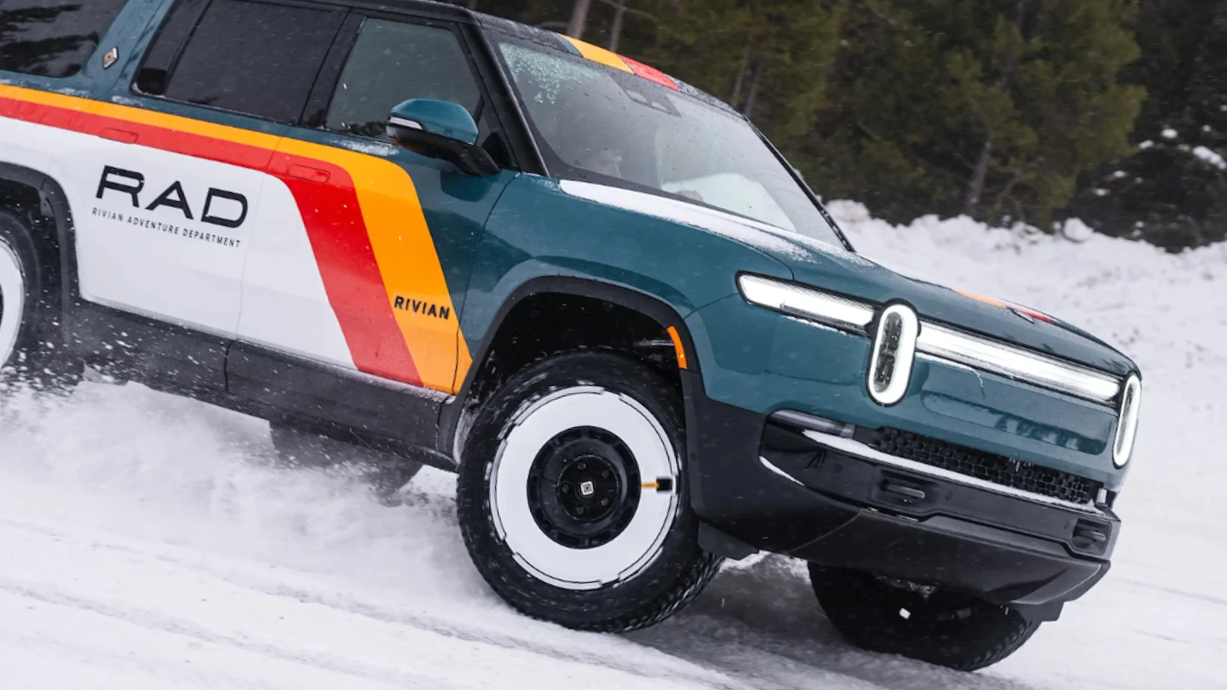 Teal and white Rivian electric truck with red and yellow stripes driving on snow.