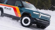 Teal and white Rivian electric truck with red and yellow stripes driving on snow.