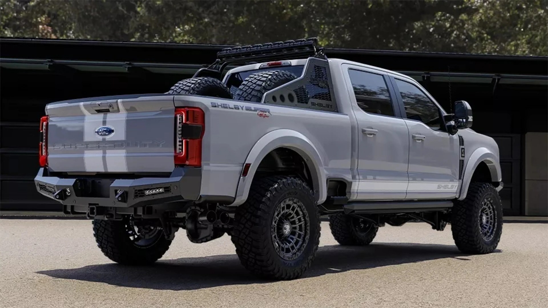 White Ford Shelby Super Duty pickup truck with off-road tires and two spare tires mounted in the bed.