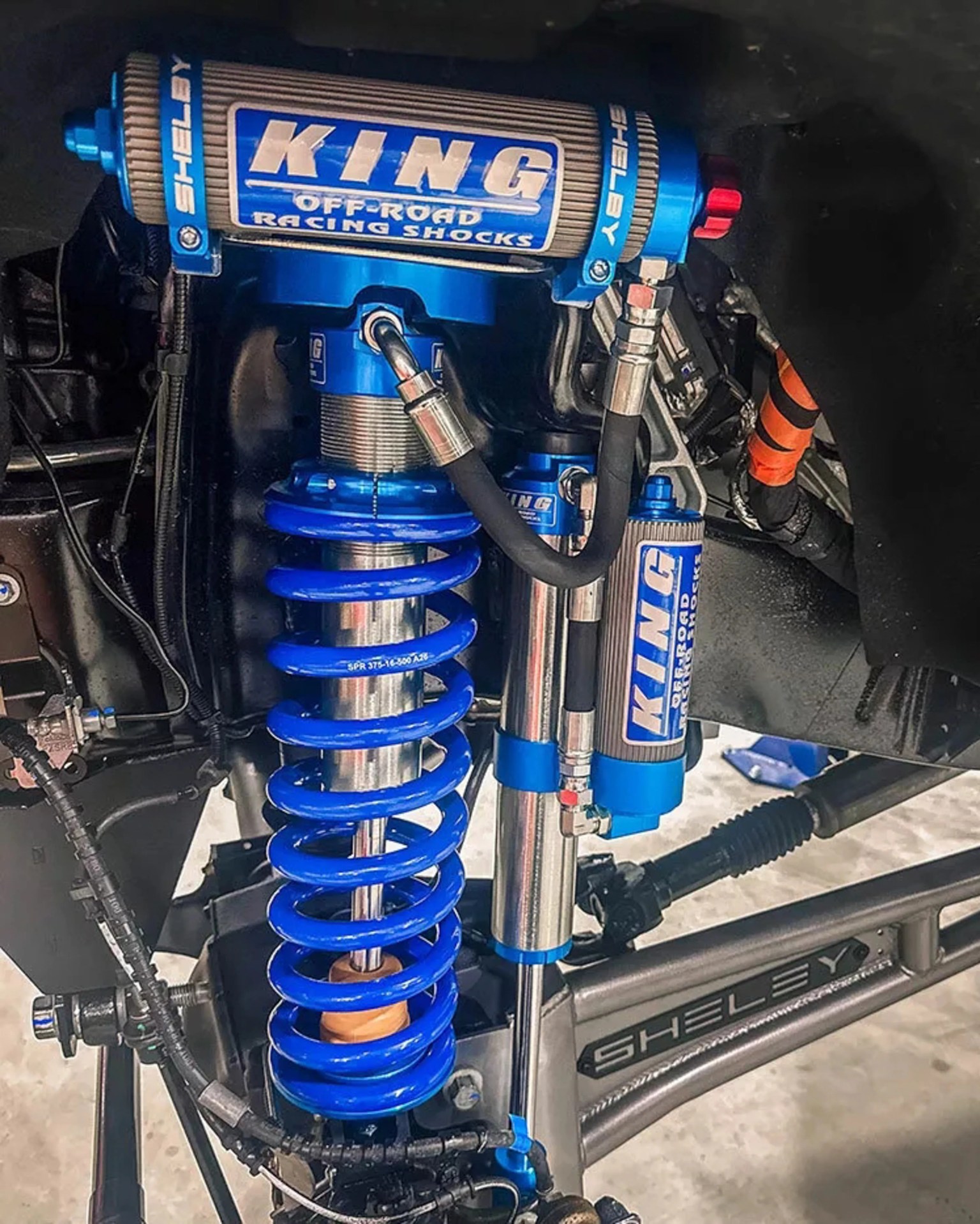 Blue King off-road racing shock absorber with coil spring and Shelby-branded suspension arm.