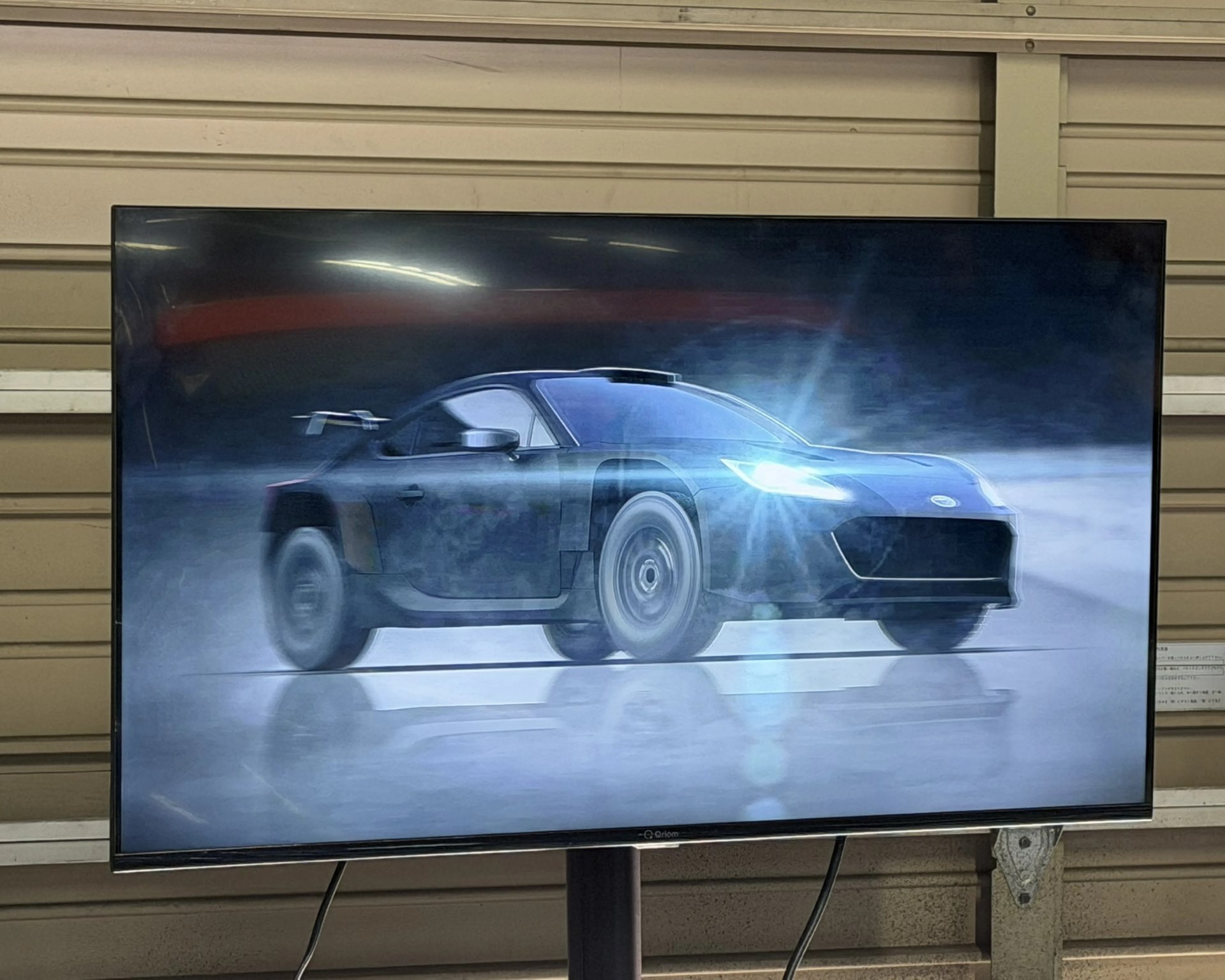 Flat-screen TV displaying a digital image of a blue sports car with headlights on, set against a dark, misty background.