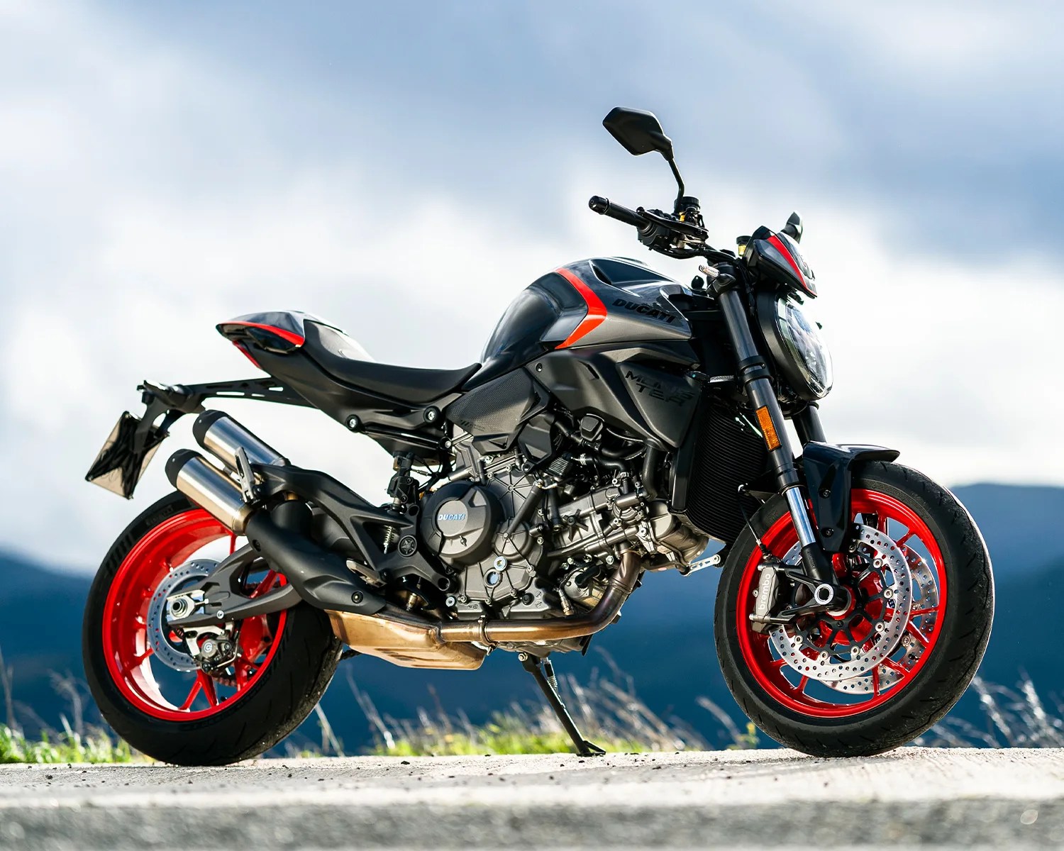 Black and gray Ducati motorcycle with red wheels parked outdoors on a road.