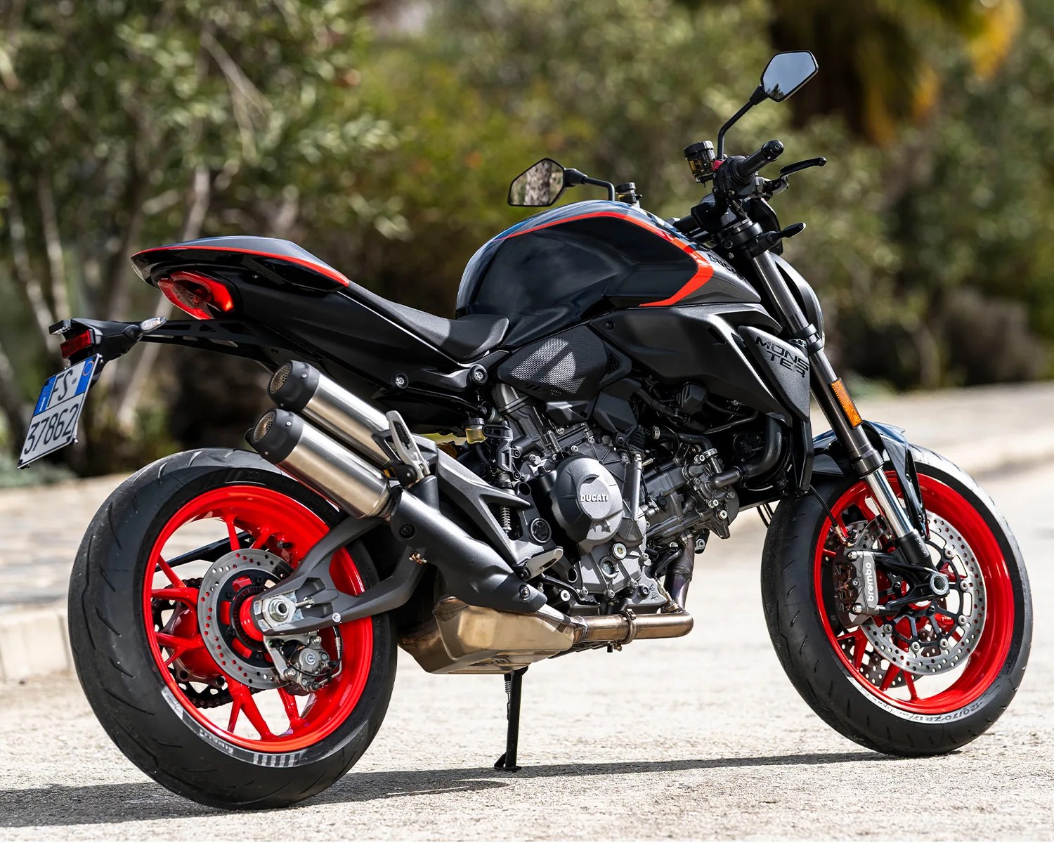 Black Ducati Monster motorcycle with red rims parked on a paved road.