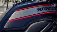 Close-up of a black Honda motorcycle fuel tank with red and gray stripes and the Honda logo.