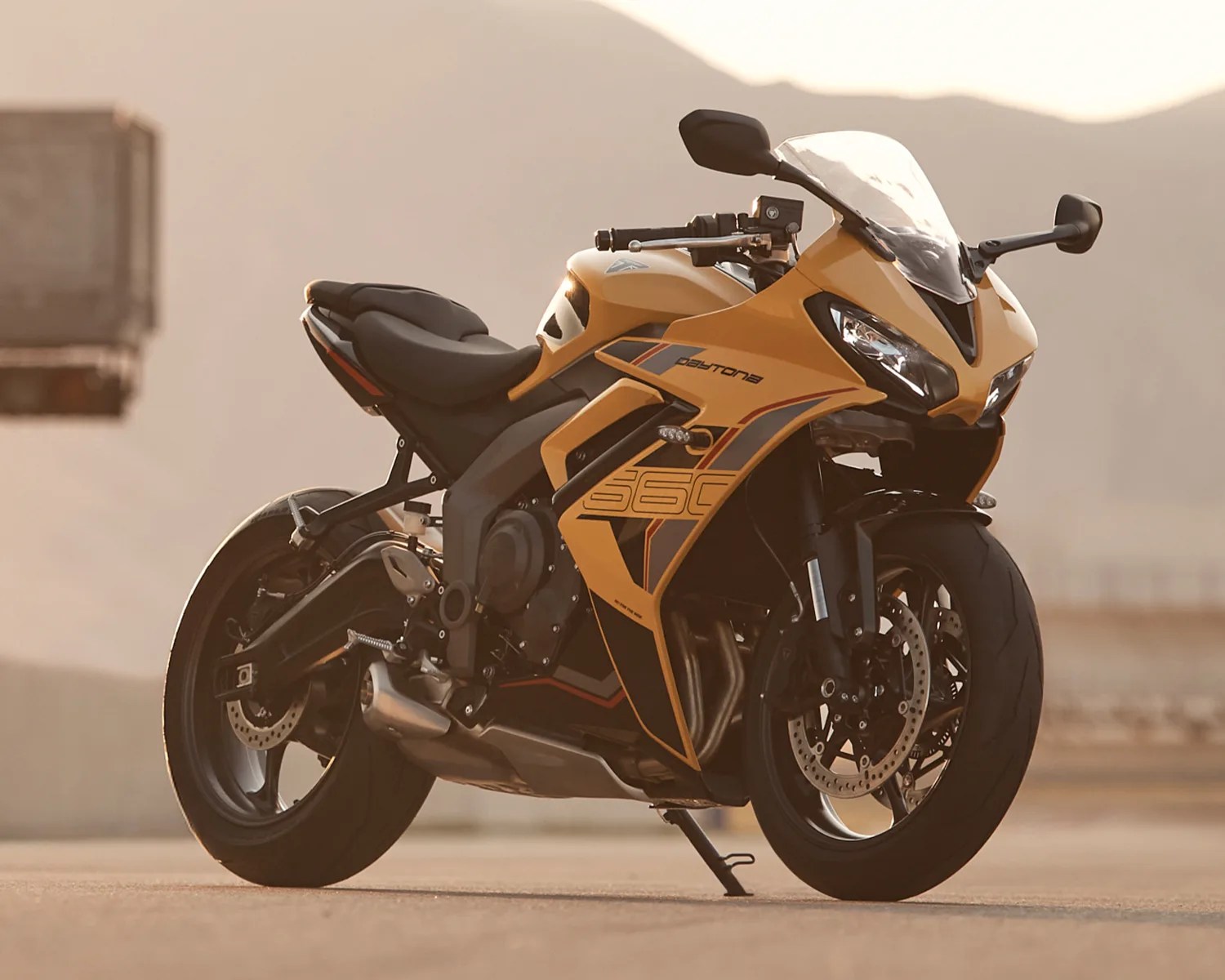 Yellow and black Triumph Daytona 660 sport motorcycle parked on a road with mountains in the background.