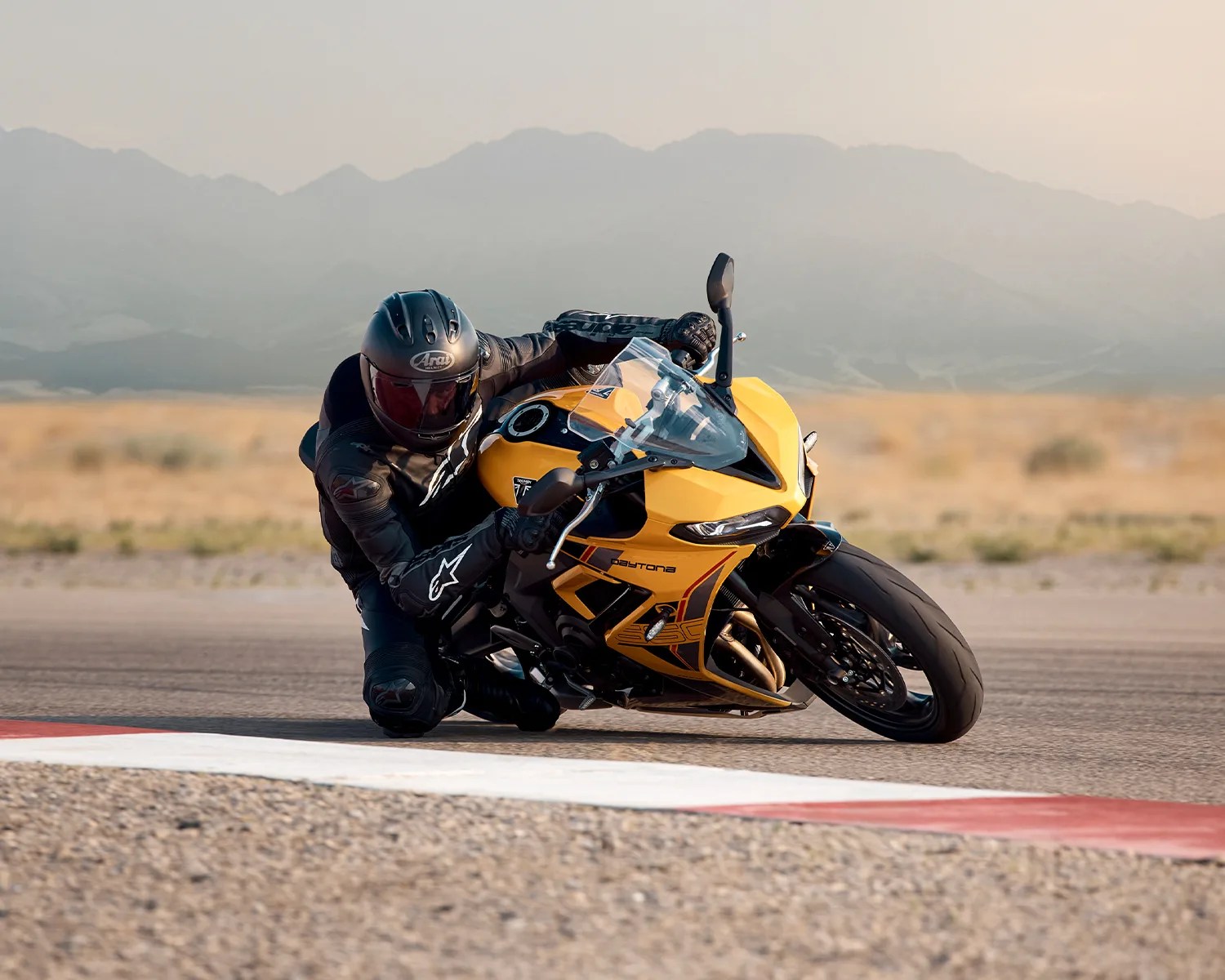 Motorcyclist in black gear leaning into a turn on a yellow Triumph Daytona motorcycle on a racetrack.