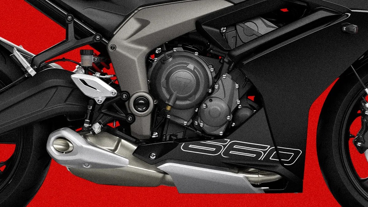 Close-up of a black and gray motorcycle engine and exhaust system with "660" decal on the fairing against a red background.