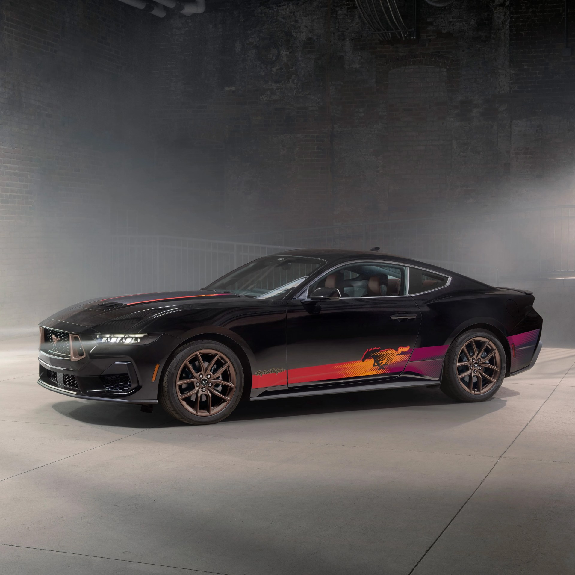Black Ford Mustang with bronze wheels and red-orange-pink gradient side decal in a foggy industrial setting.