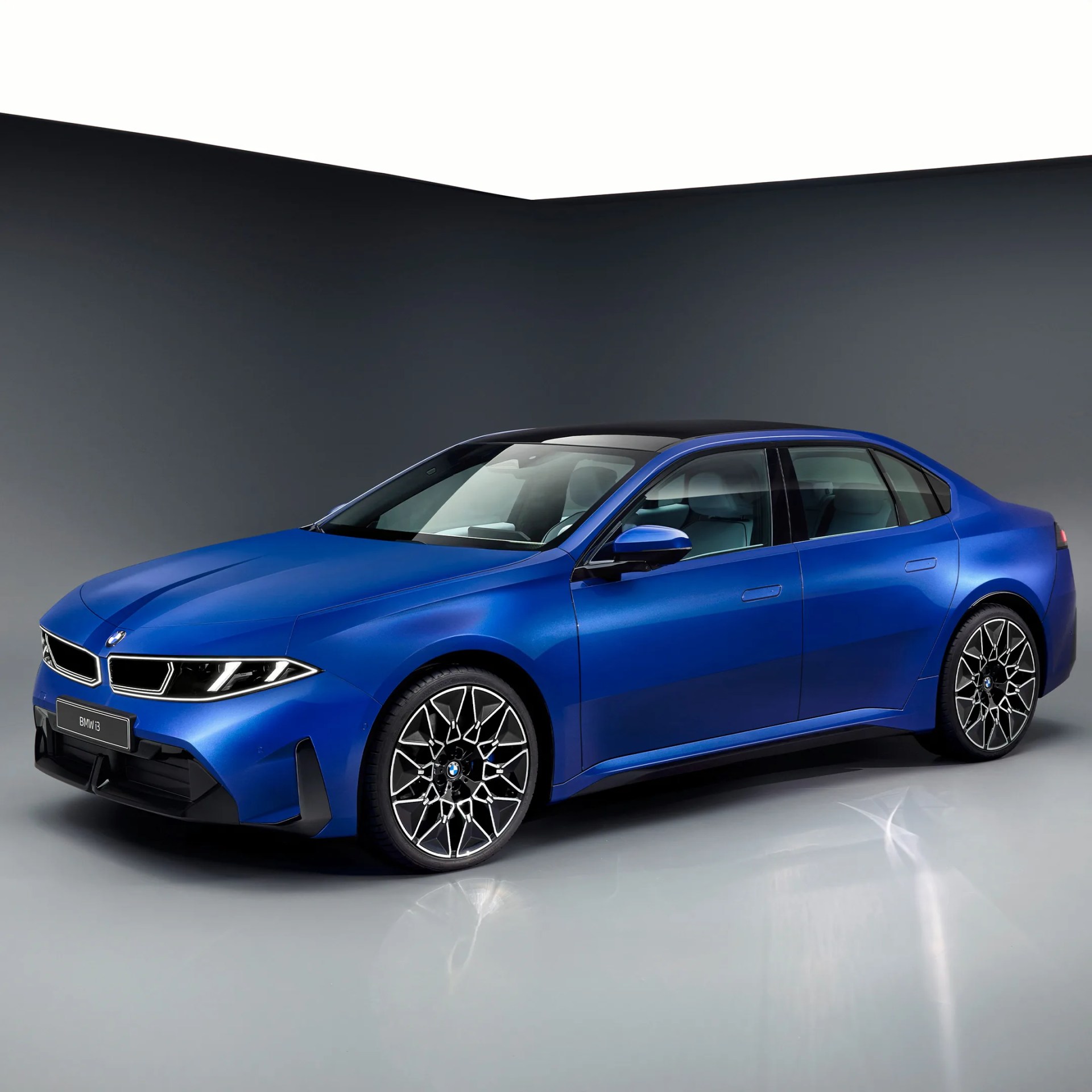 Blue BMW i3 sedan with black roof and intricate alloy wheels in a studio setting.