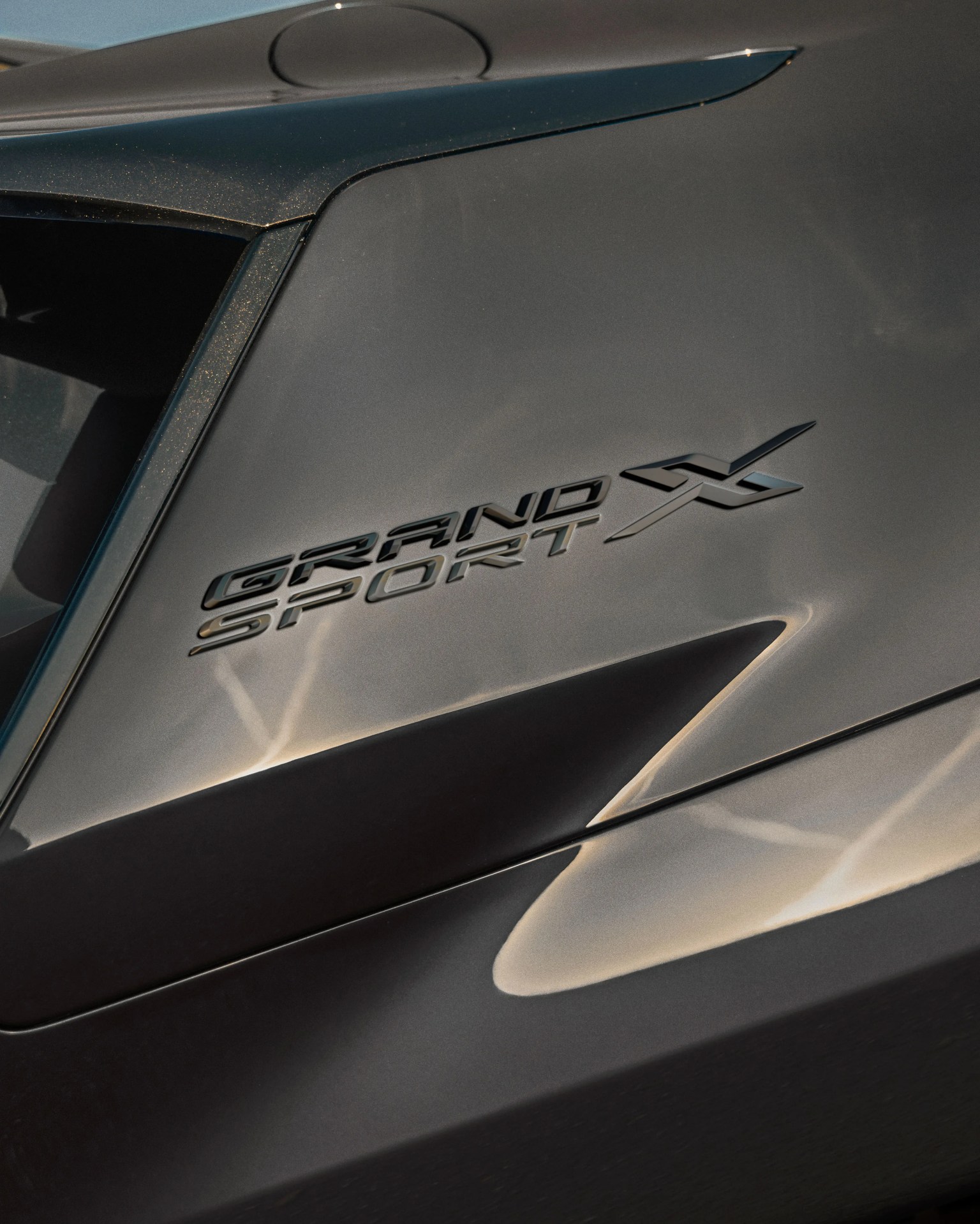 Close-up of a metallic gray car panel with "Grand Sport X" emblem in black lettering.