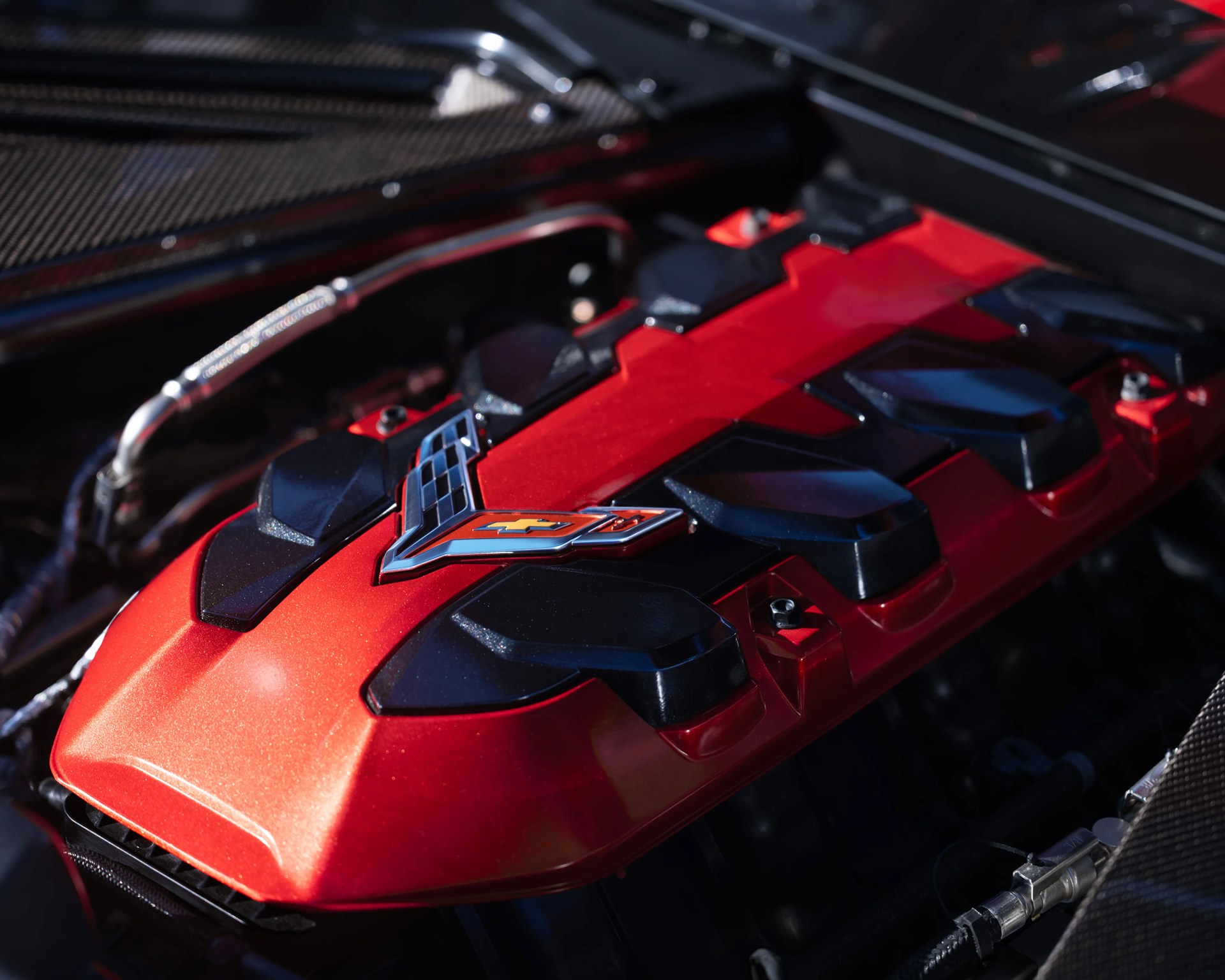 Red and black Chevrolet Corvette engine cover with emblem under car hood.