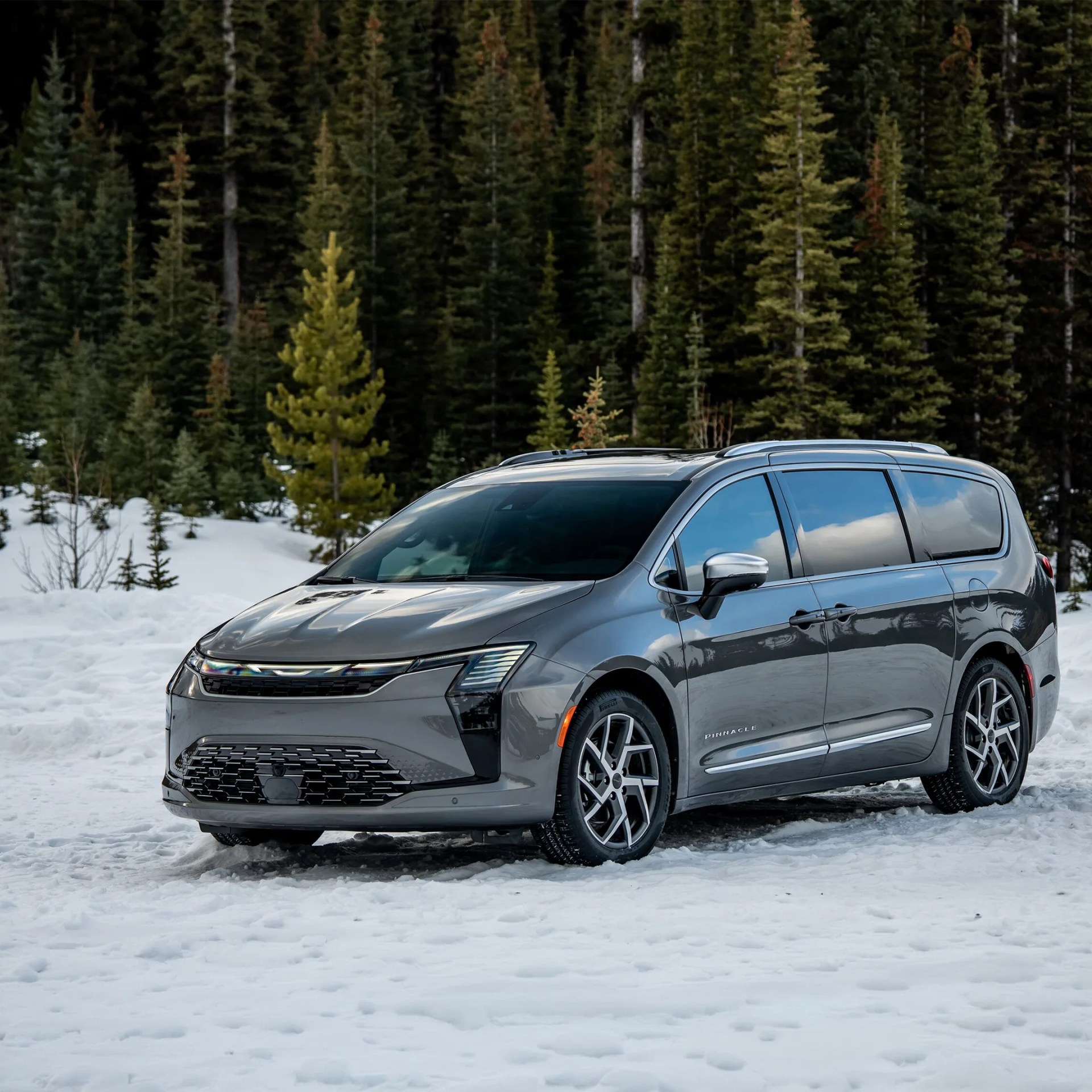 Gray Chrysler minivan parked on snow with evergreen trees in the background.