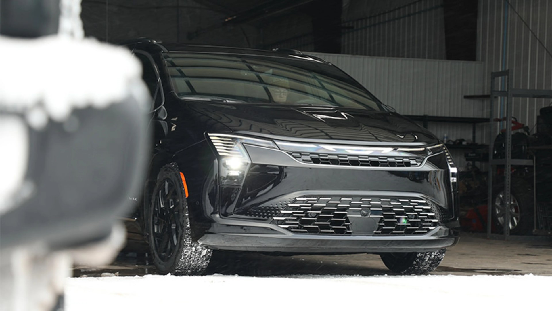 Black modern electric SUV with LED headlights parked inside a garage with snow on the ground.