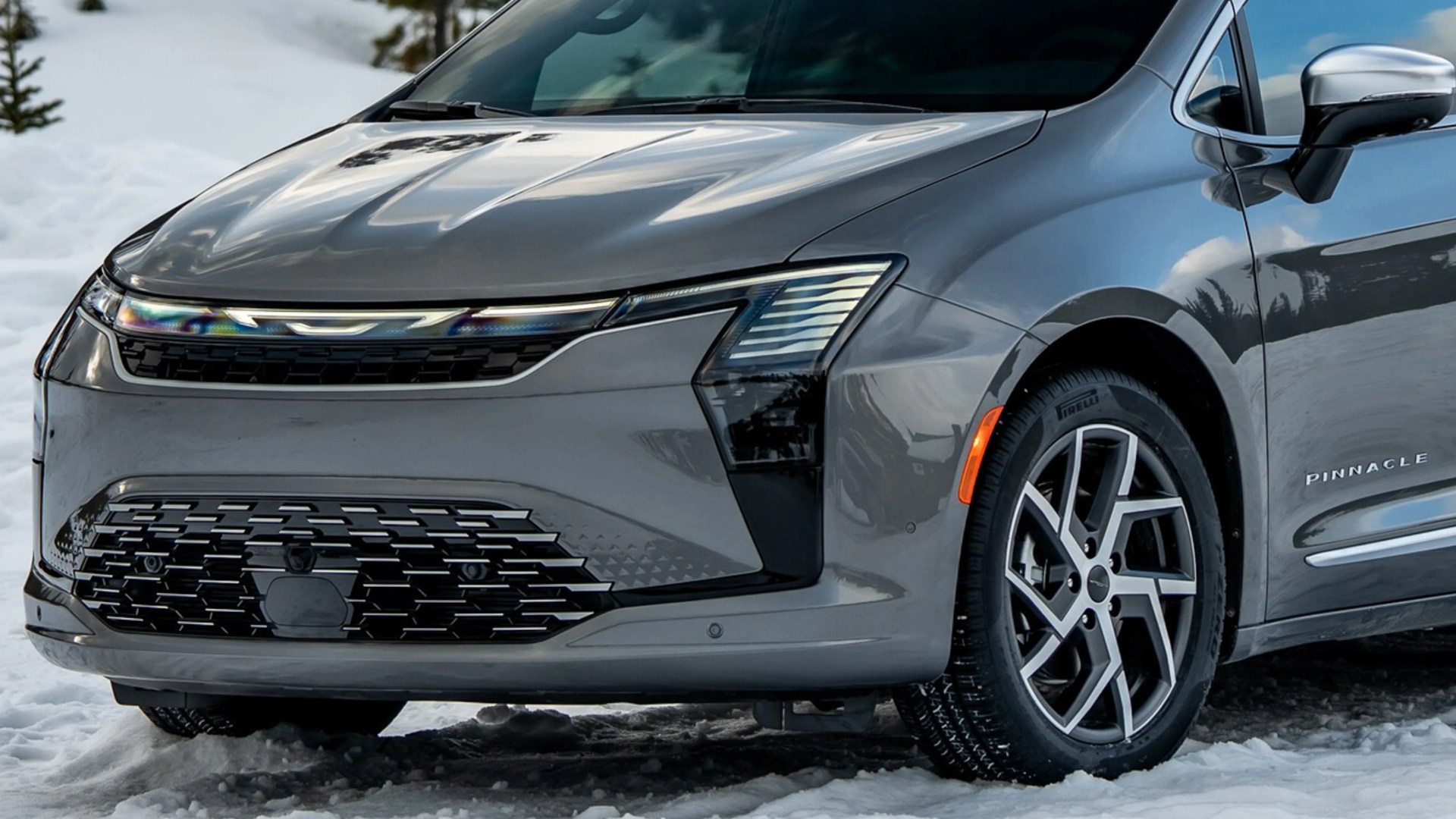 Front side view of a gray electric car with distinctive LED headlights and a black grille on snow.
