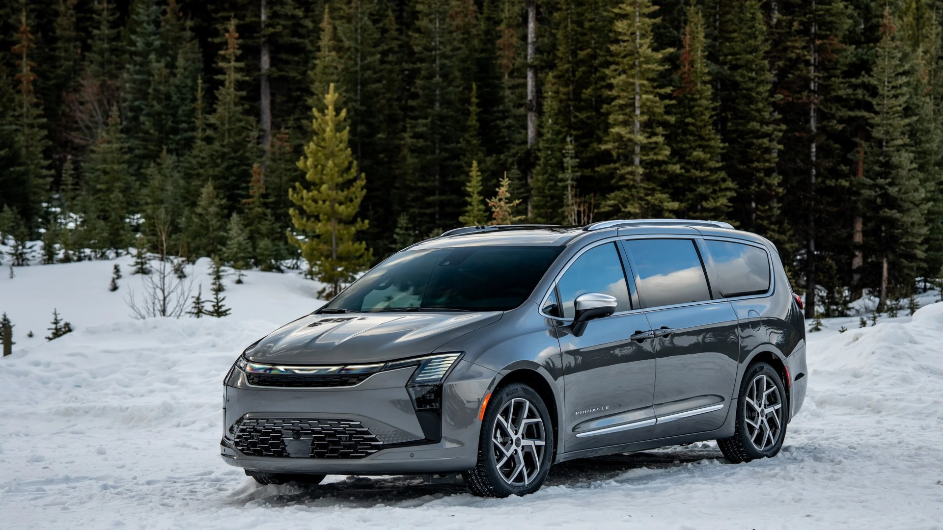 Gray Chrysler minivan with "Pinnacle" badge parked on snow with pine trees in the background.