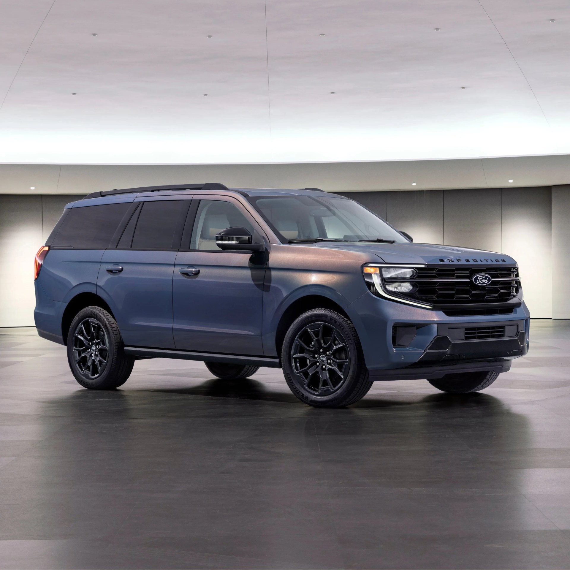 Blue Ford Expedition SUV with black wheels parked indoors on a polished floor.
