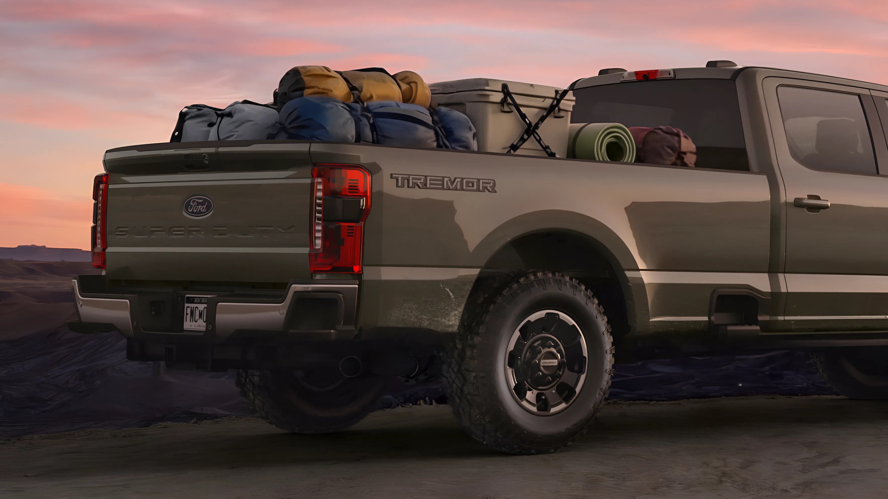 Olive green Ford Tremor Super Duty pickup truck loaded with camping gear in the bed at sunset.