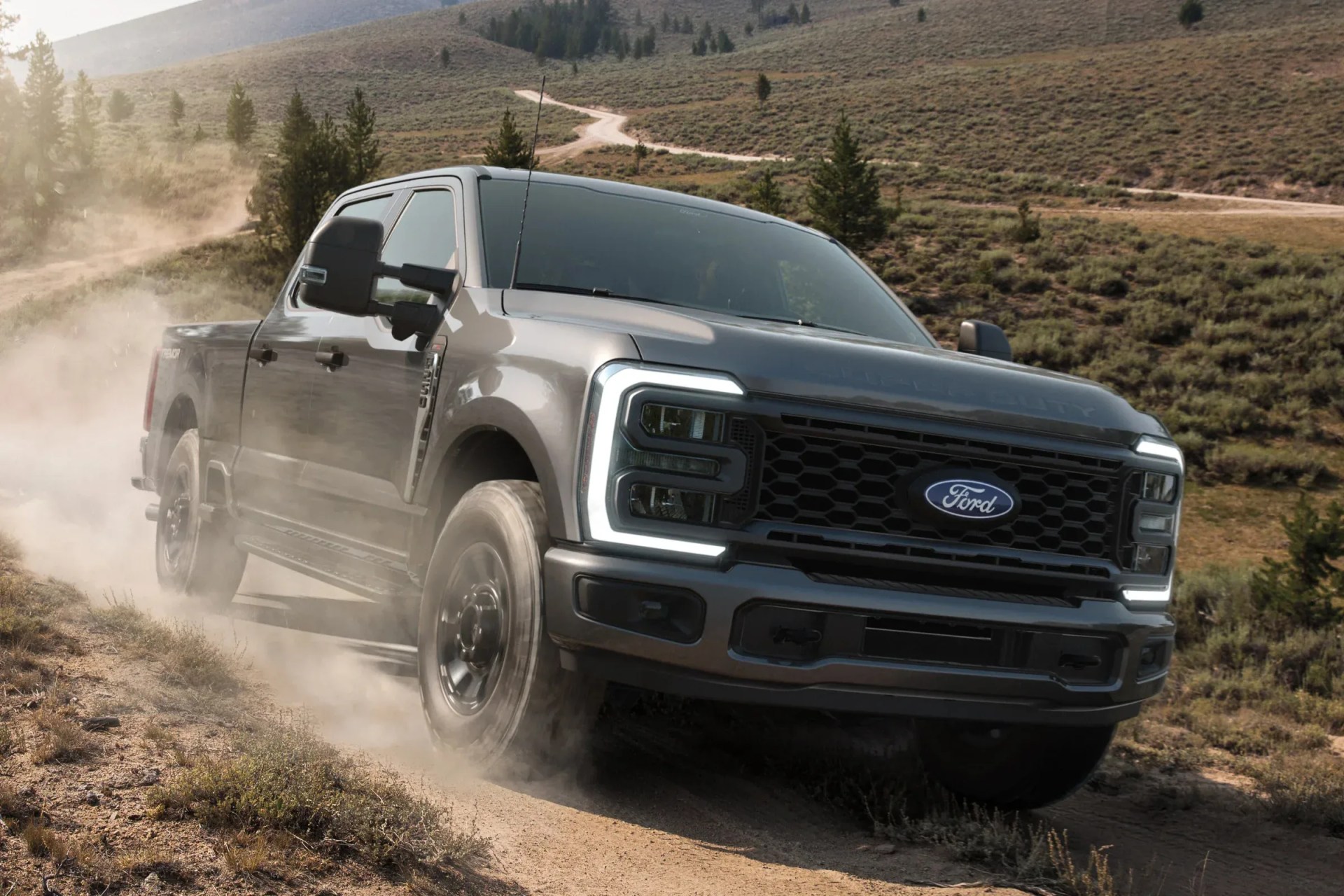 Gray Ford pickup truck driving off-road on a dusty dirt path with illuminated LED headlights.