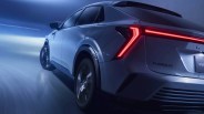 Rear-side view of a silver electric SUV with illuminated red taillights driving on a wet road at night.