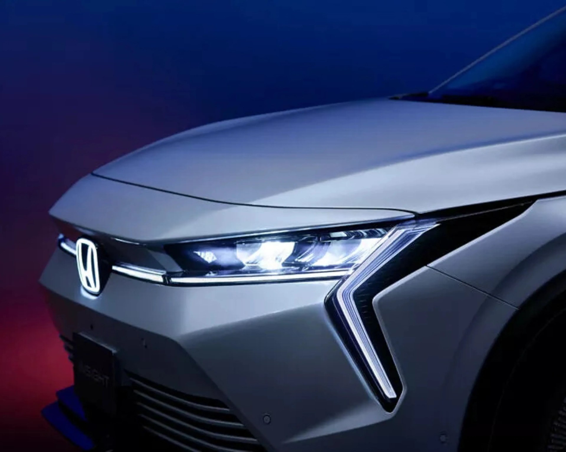 Front left side of a silver Honda car with illuminated headlights and LED daytime running lights in a dark setting.