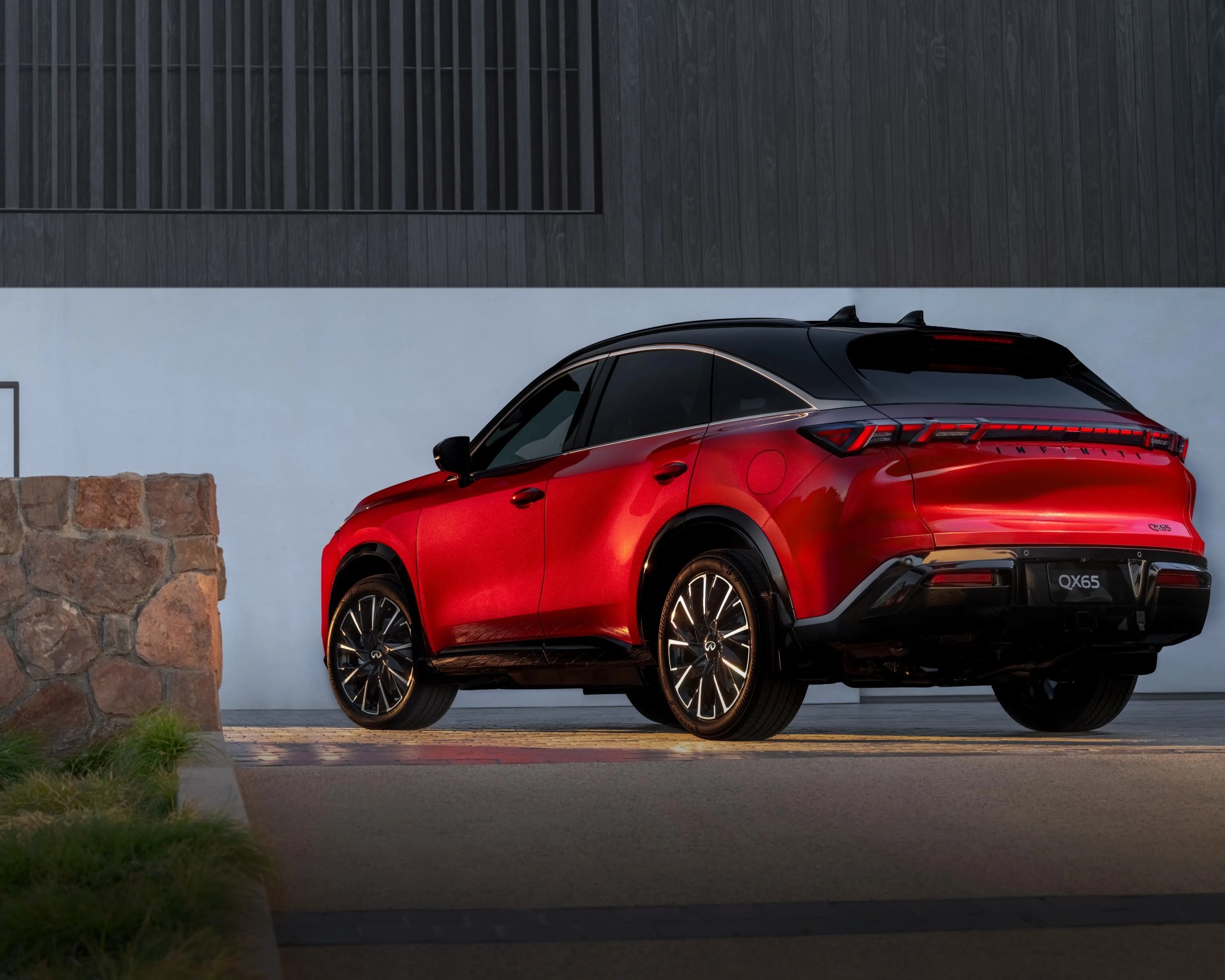 Red Infiniti QX65 SUV with black roof and illuminated wheels parked near a stone wall and modern building.