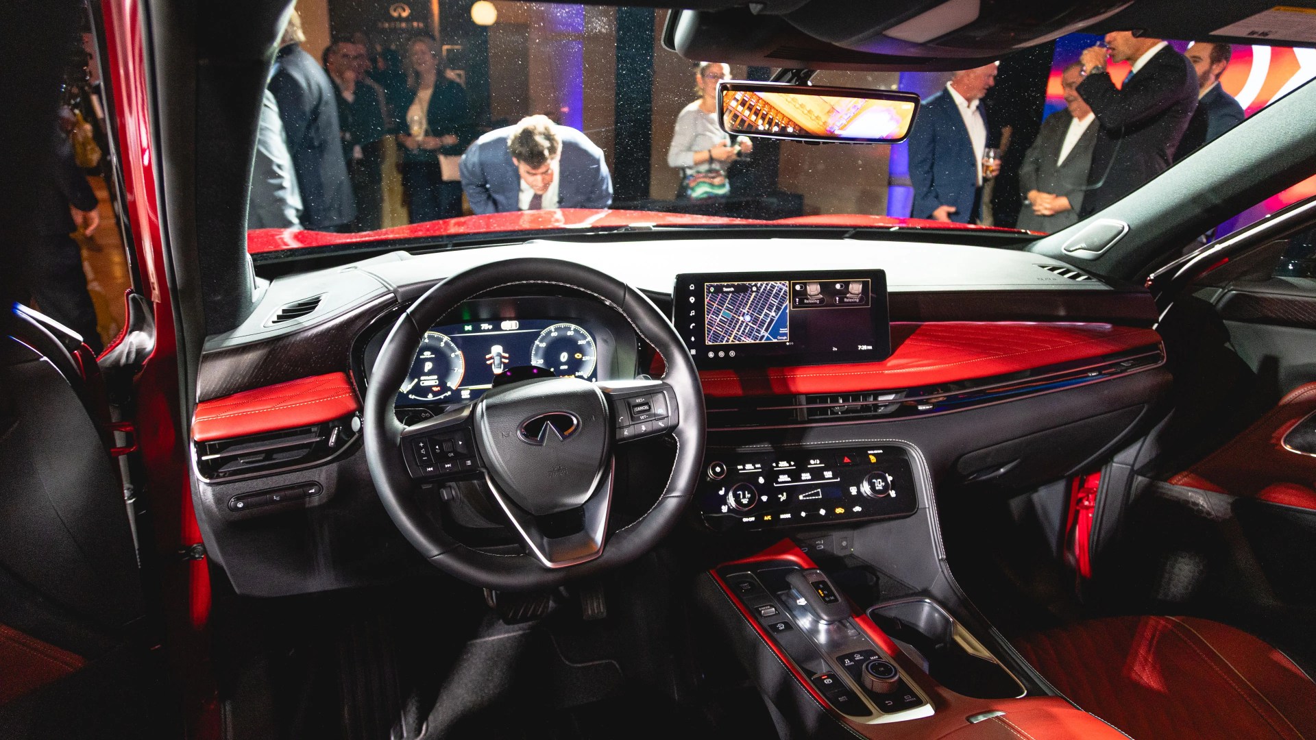 Interior of a red Infiniti car showing a black leather steering wheel, digital dashboard, and red and black leather dashboard and seats.