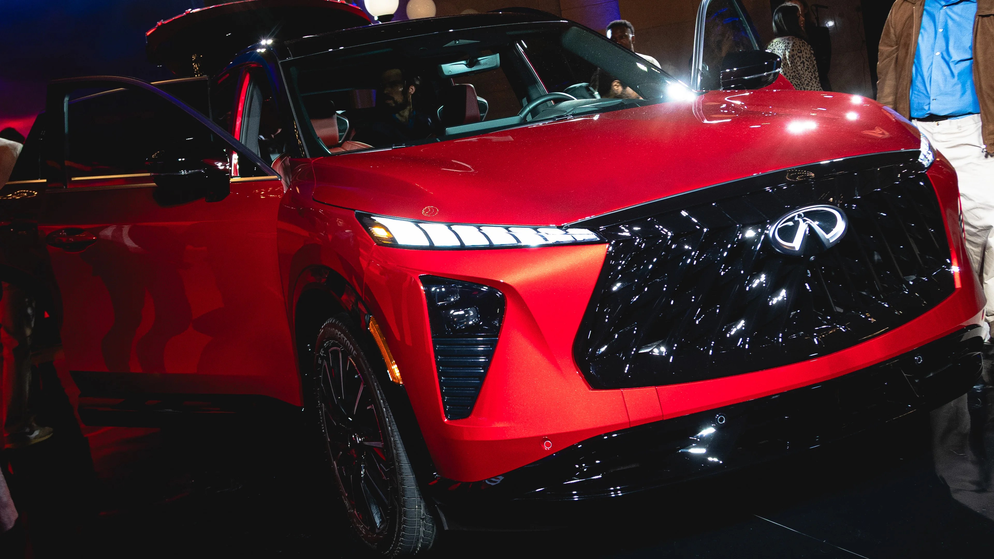 Red Infiniti SUV with black grille and LED headlights, front passenger door open, shown indoors.