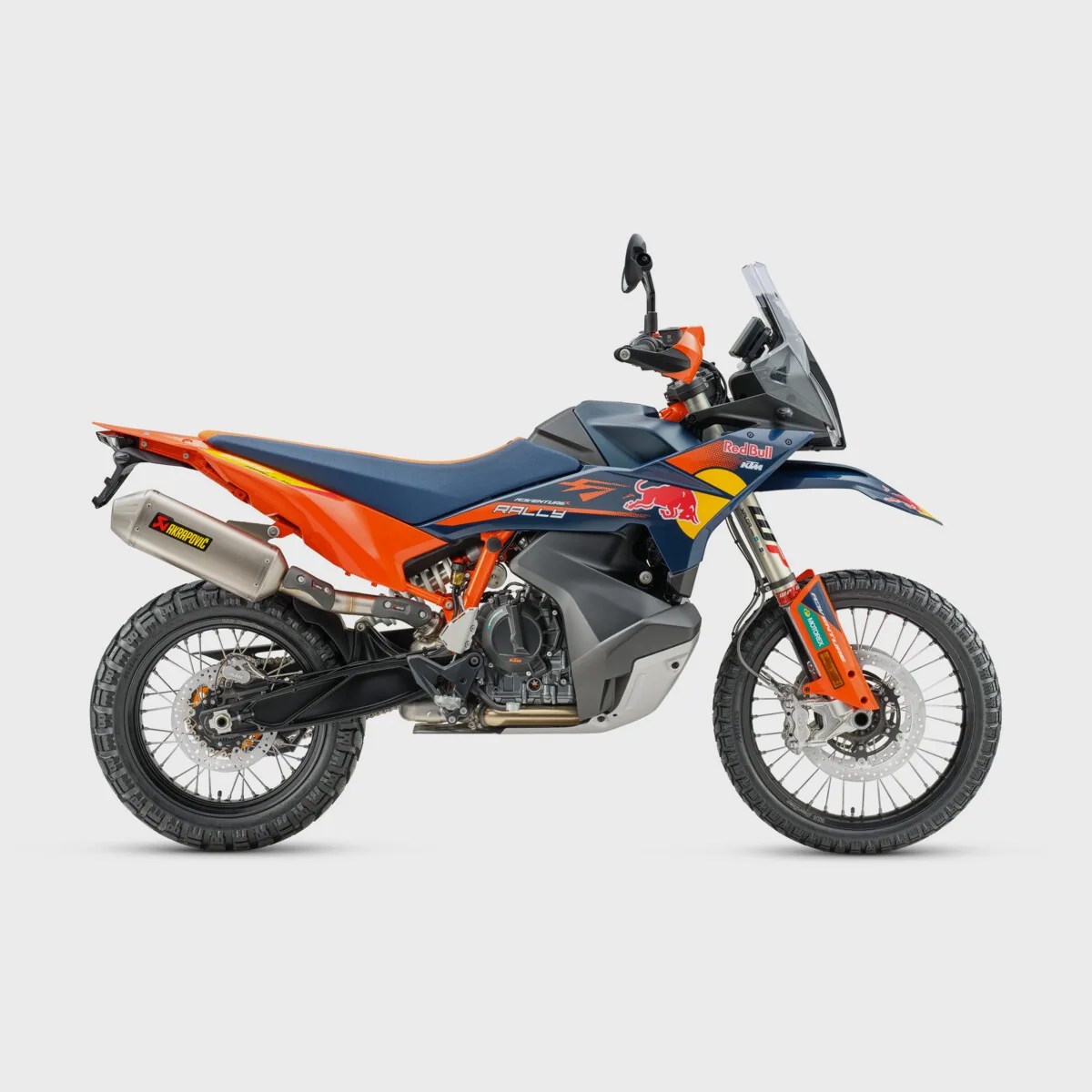 Orange and blue KTM rally motorcycle with Red Bull branding and off-road tires on a white background.