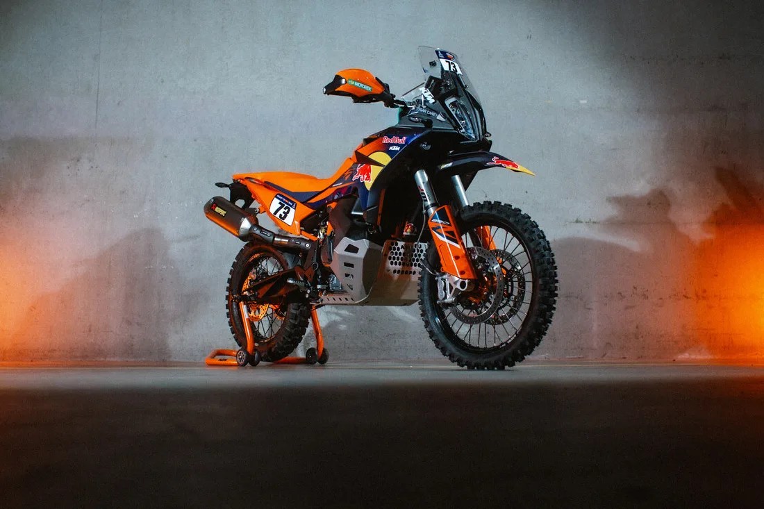 Orange and black KTM off-road motorcycle with knobby tires and Red Bull branding against a concrete wall.