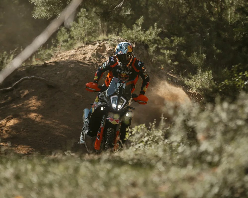 Off-road motorcycle with bright headlights ridden on a dirt trail surrounded by trees and bushes.