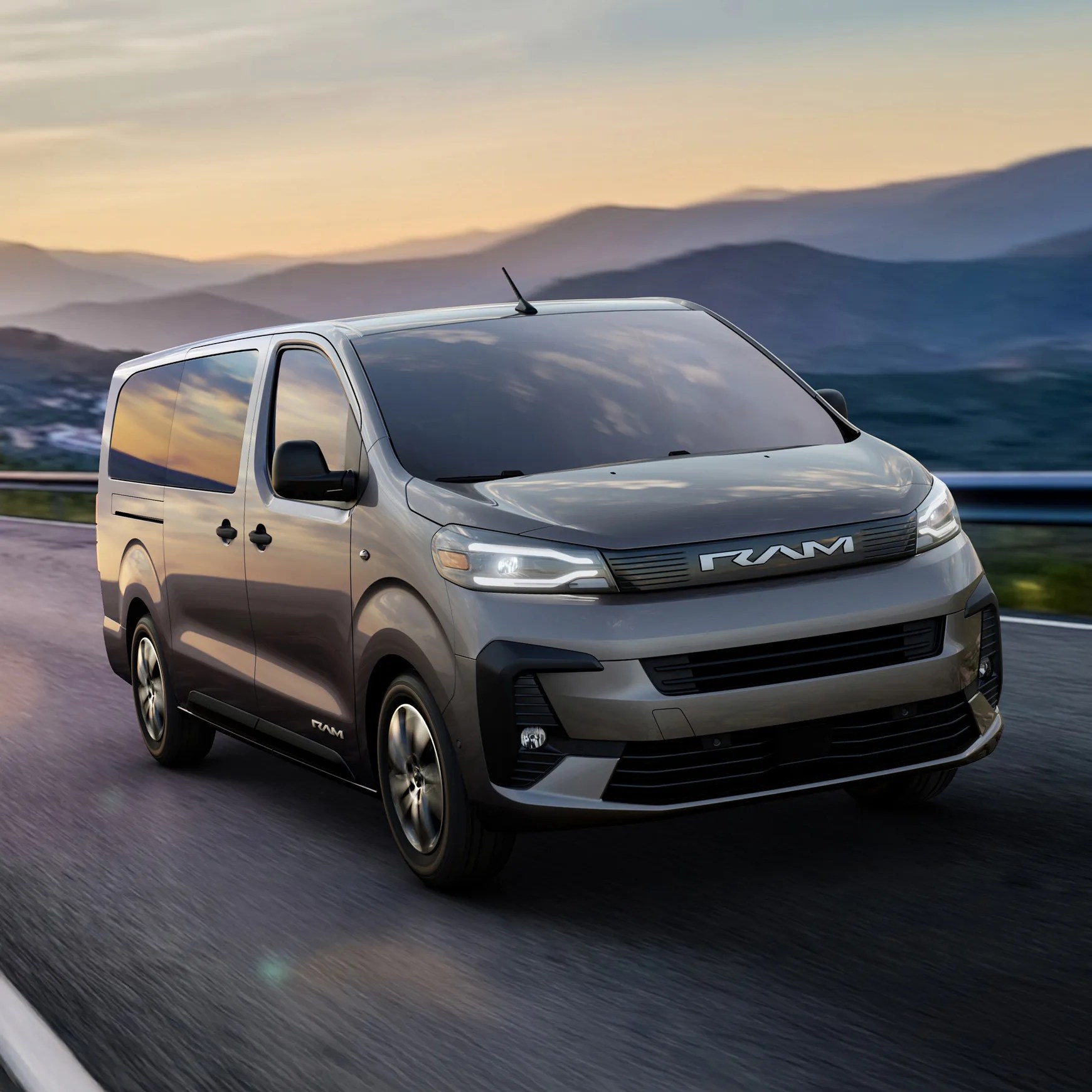 Gray RAM van with tinted windows driving on a mountain road at sunset.