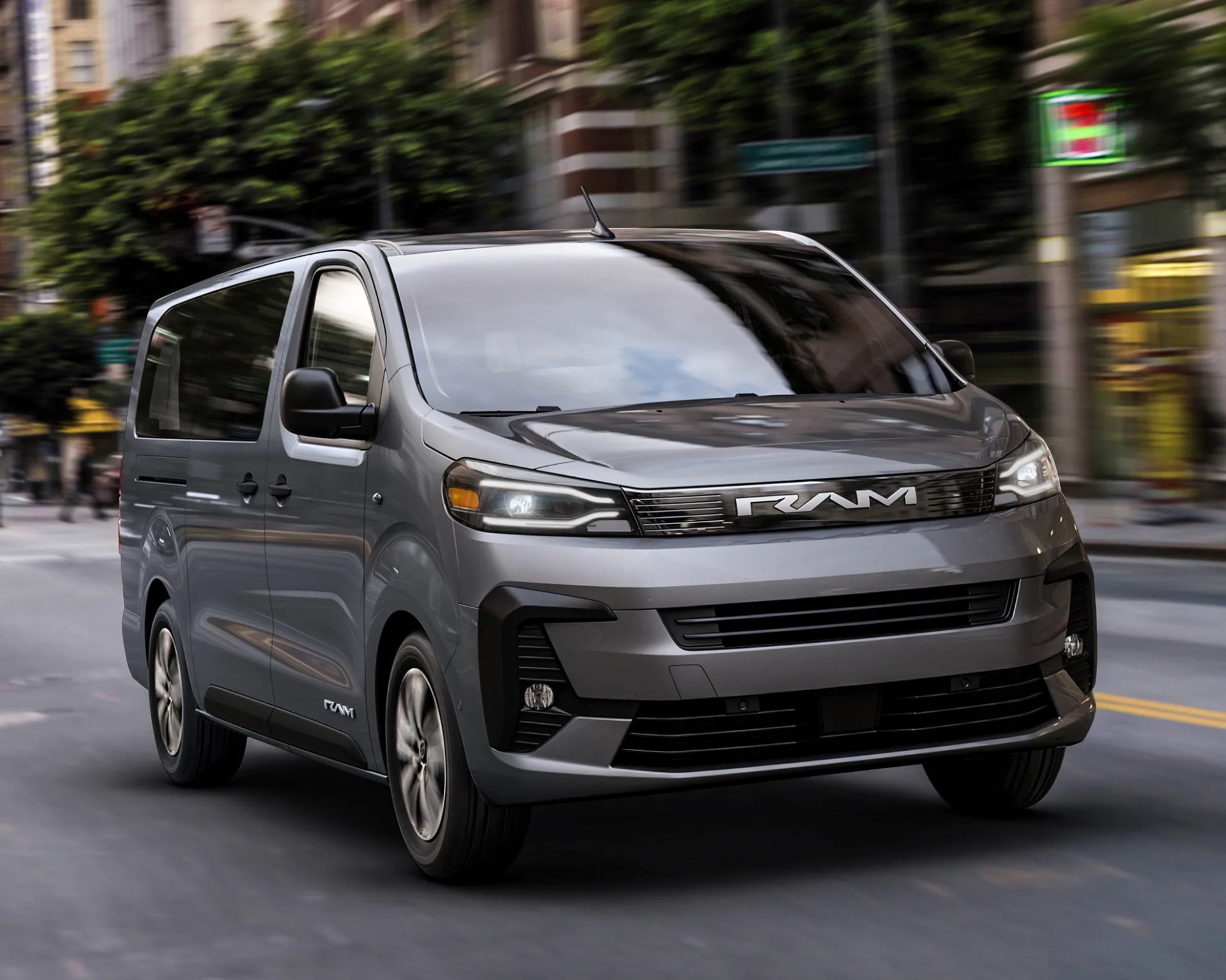 Gray RAM van with black grille and tinted windows driving on a city street.