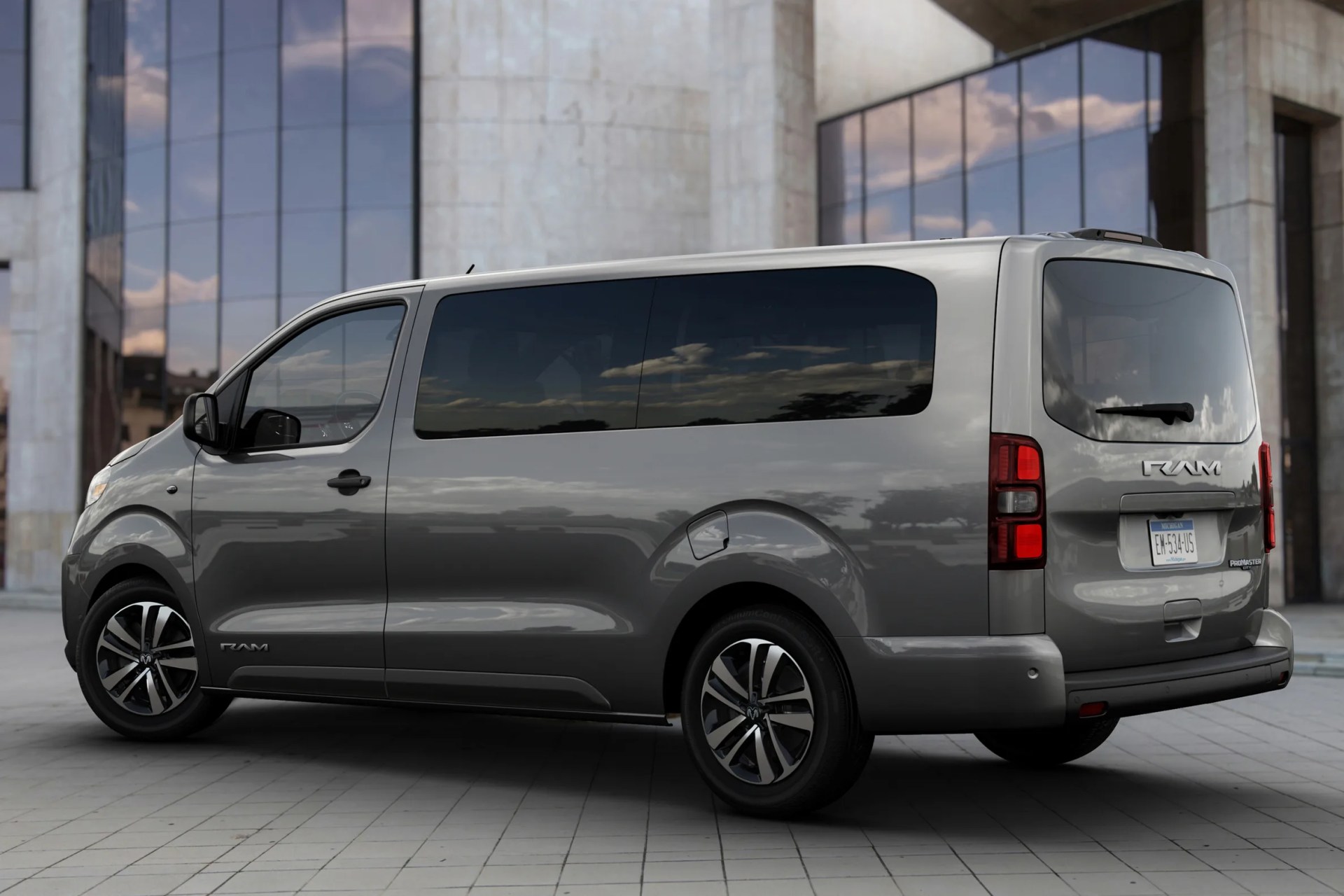 Gray RAM ProMaster van with tinted windows parked on tiled ground in front of a modern building with large glass windows.