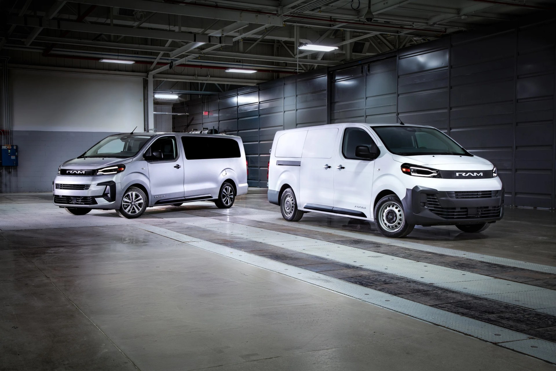 Two white RAM vans parked inside a large industrial garage with overhead lighting.