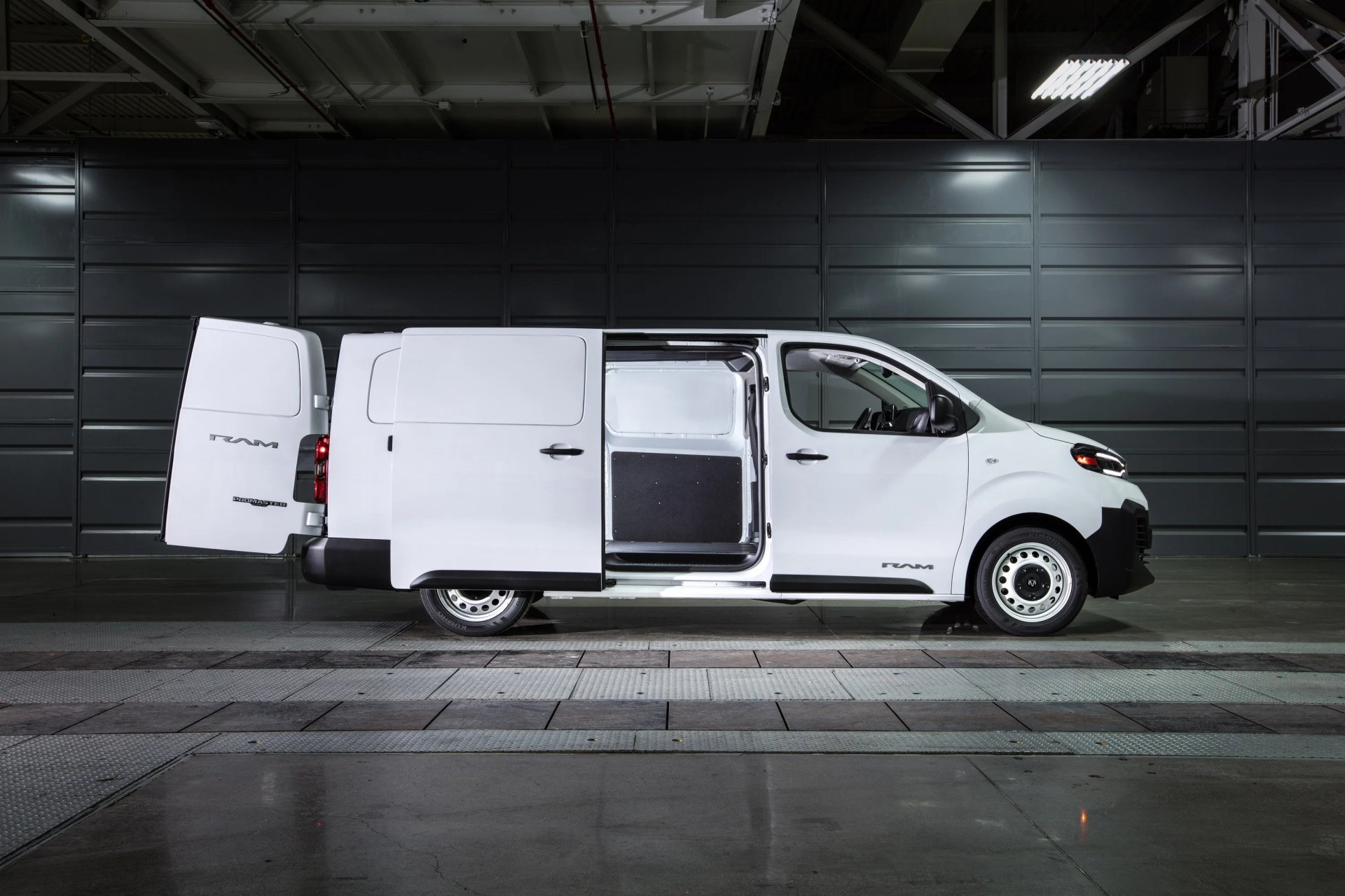 White RAM ProMaster City cargo van with rear and side doors open, parked indoors against a dark wall.