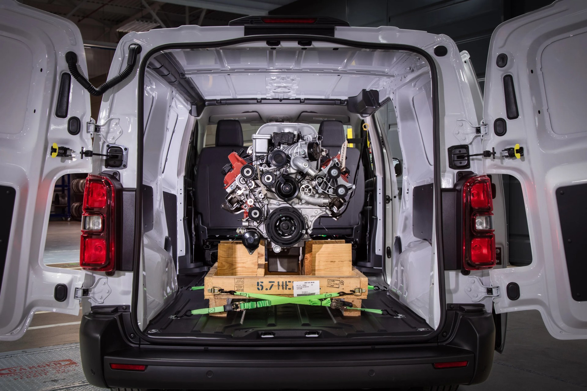 White cargo van with rear doors open showing a secured engine on a wooden pallet inside.
