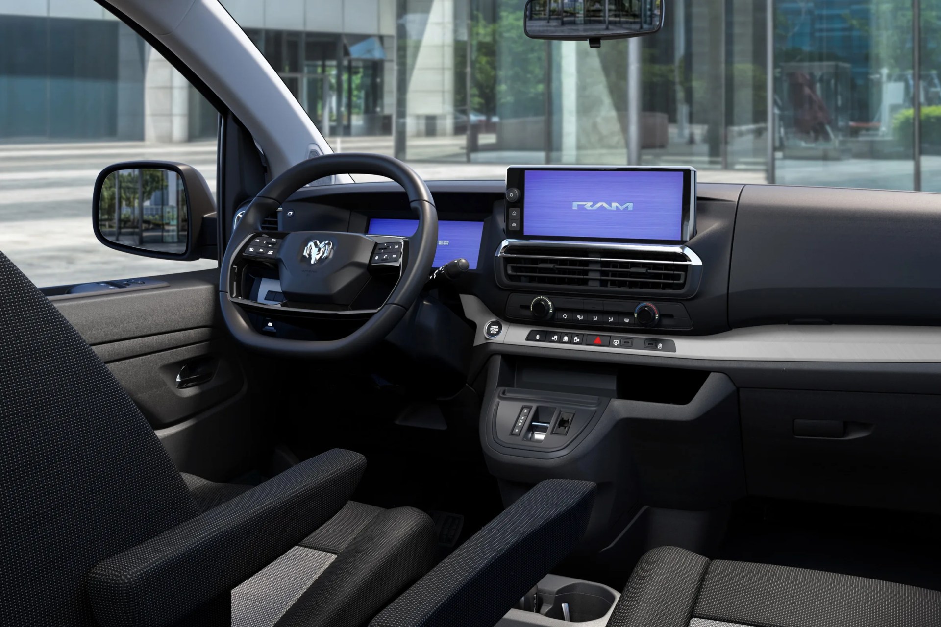 Interior of a RAM vehicle showing a black steering wheel with RAM logo, digital displays, and black fabric seats with armrests.