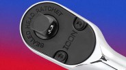 Close-up of a chrome sealed head ratchet tool with black faceplate and screws against a gradient blue to red background.