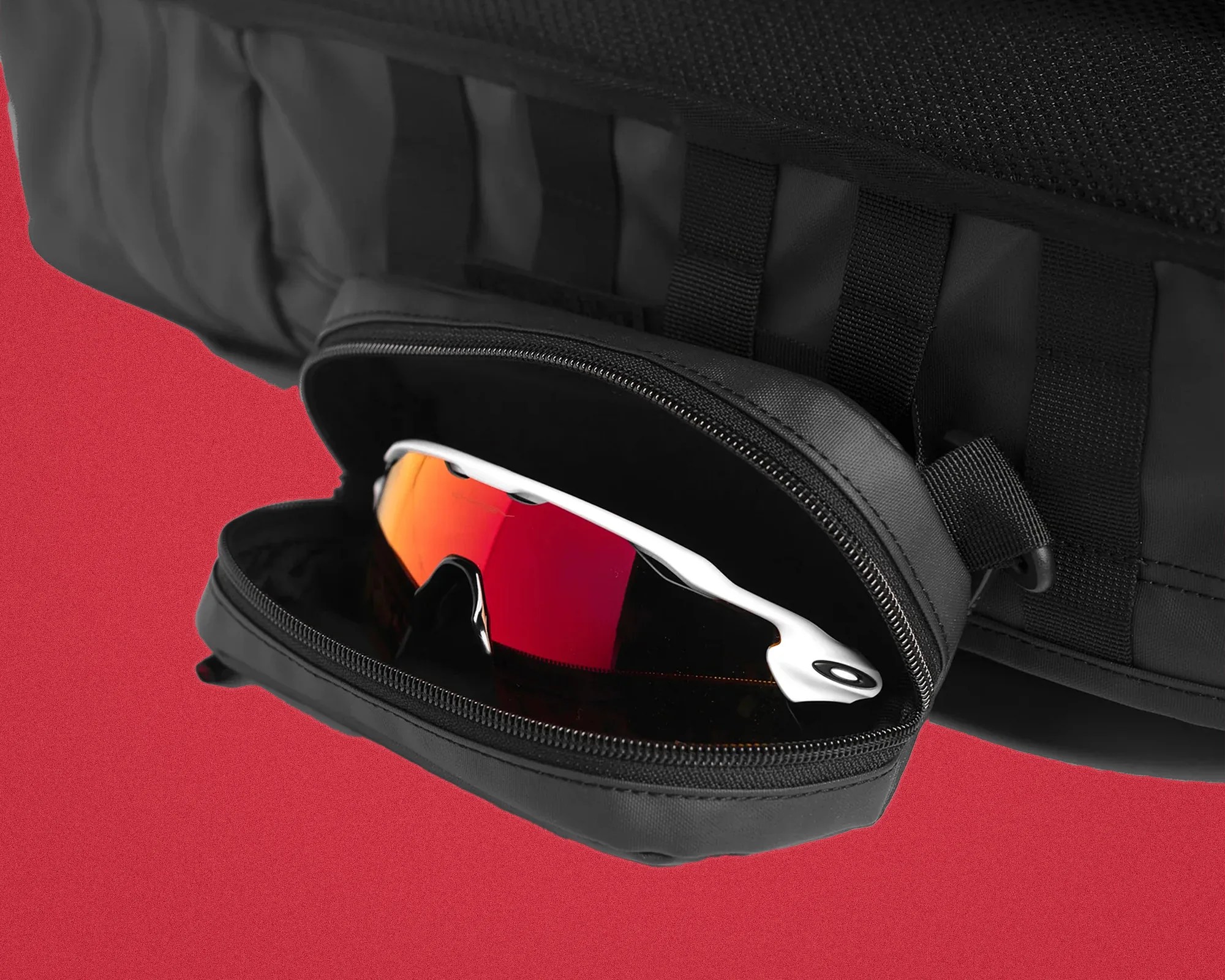 Black zippered pouch attached to a black fabric surface holding white sports sunglasses with red mirrored lenses.