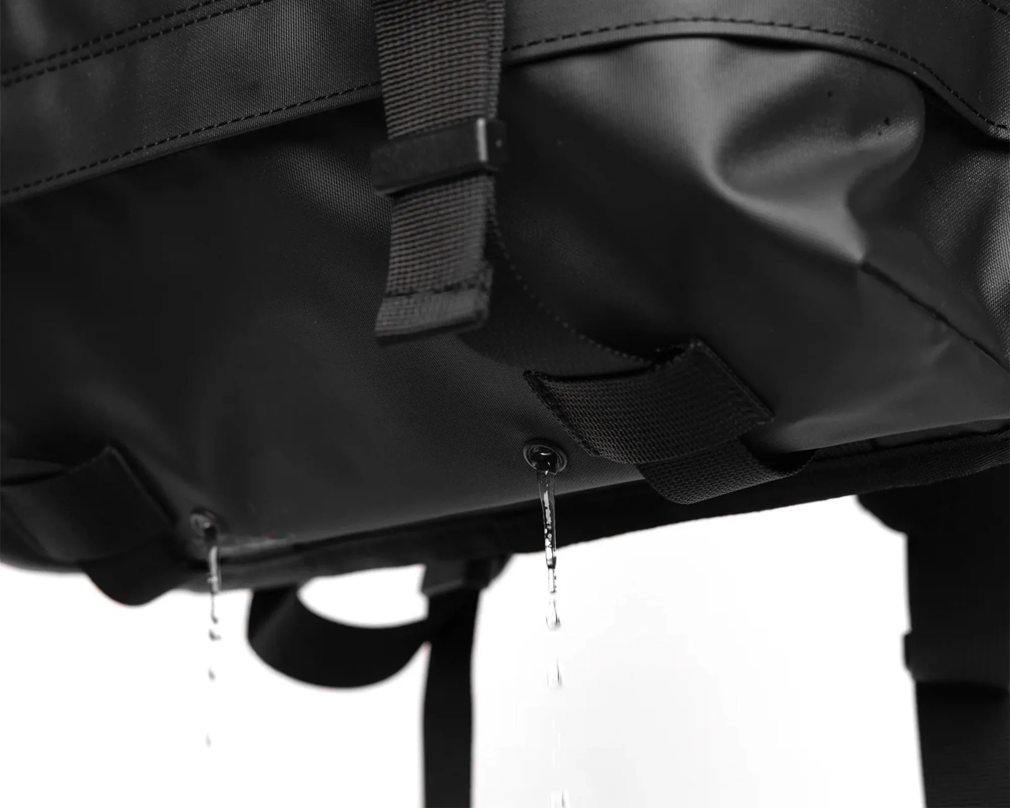 Close-up of water draining through two small holes at the bottom of a black waterproof bag.