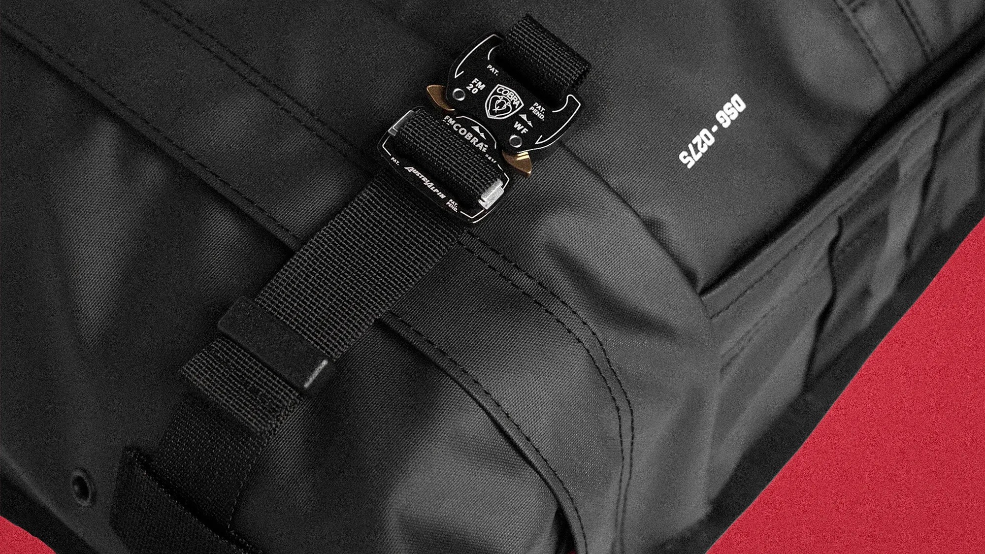 Close-up of a black fabric bag with a black Cobra buckle and strap on a red background.