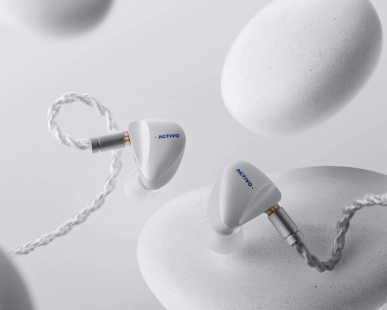 White Activo in-ear wired earphones with braided cables resting on white textured stones.