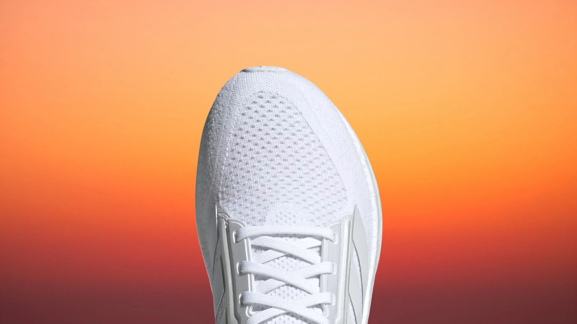 Close-up of the front part of a white athletic shoe with mesh upper and laces against an orange gradient background.