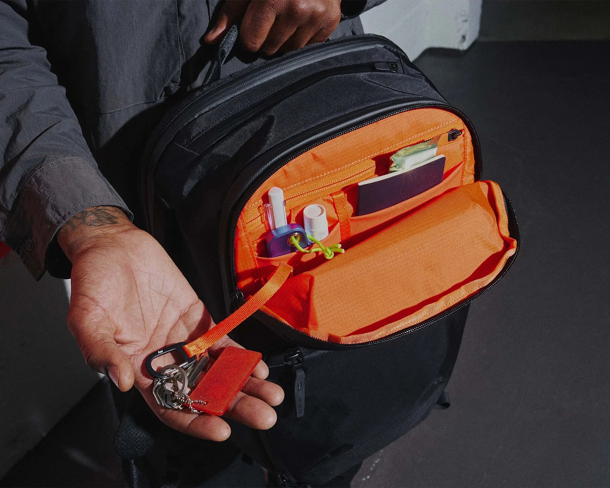 Black backpack with bright orange interior organizer holding keys, small bottles, and a notebook, held open by a person.