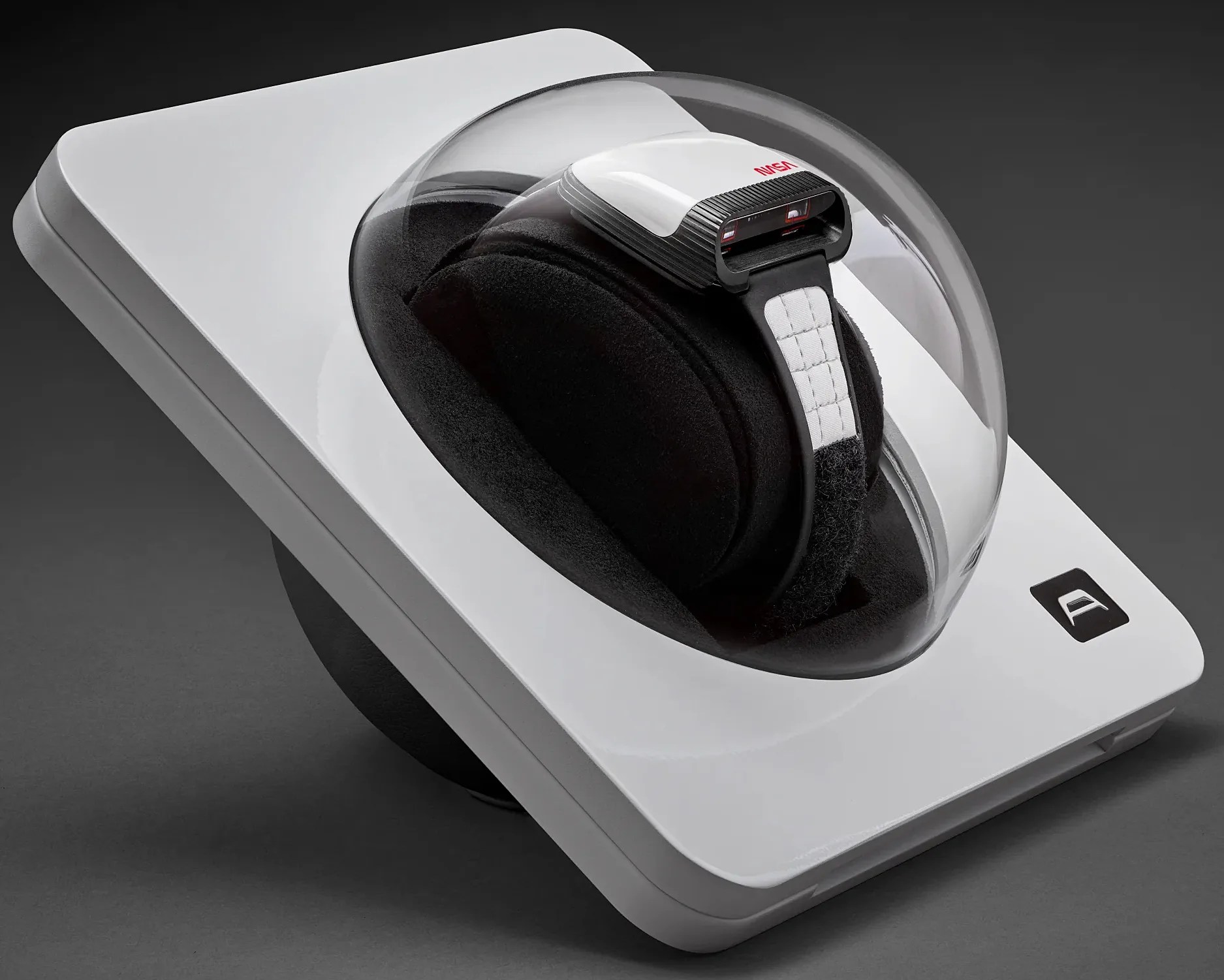 White and black NASA-branded virtual reality headset with a padded strap inside a clear dome on a white base.