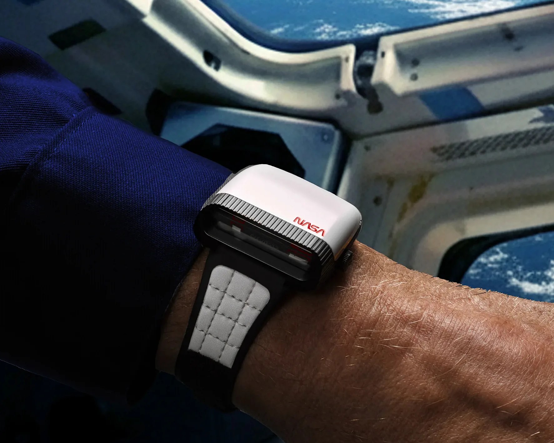 White NASA-branded smartwatch with black and white padded strap worn on a wrist inside a spacecraft.