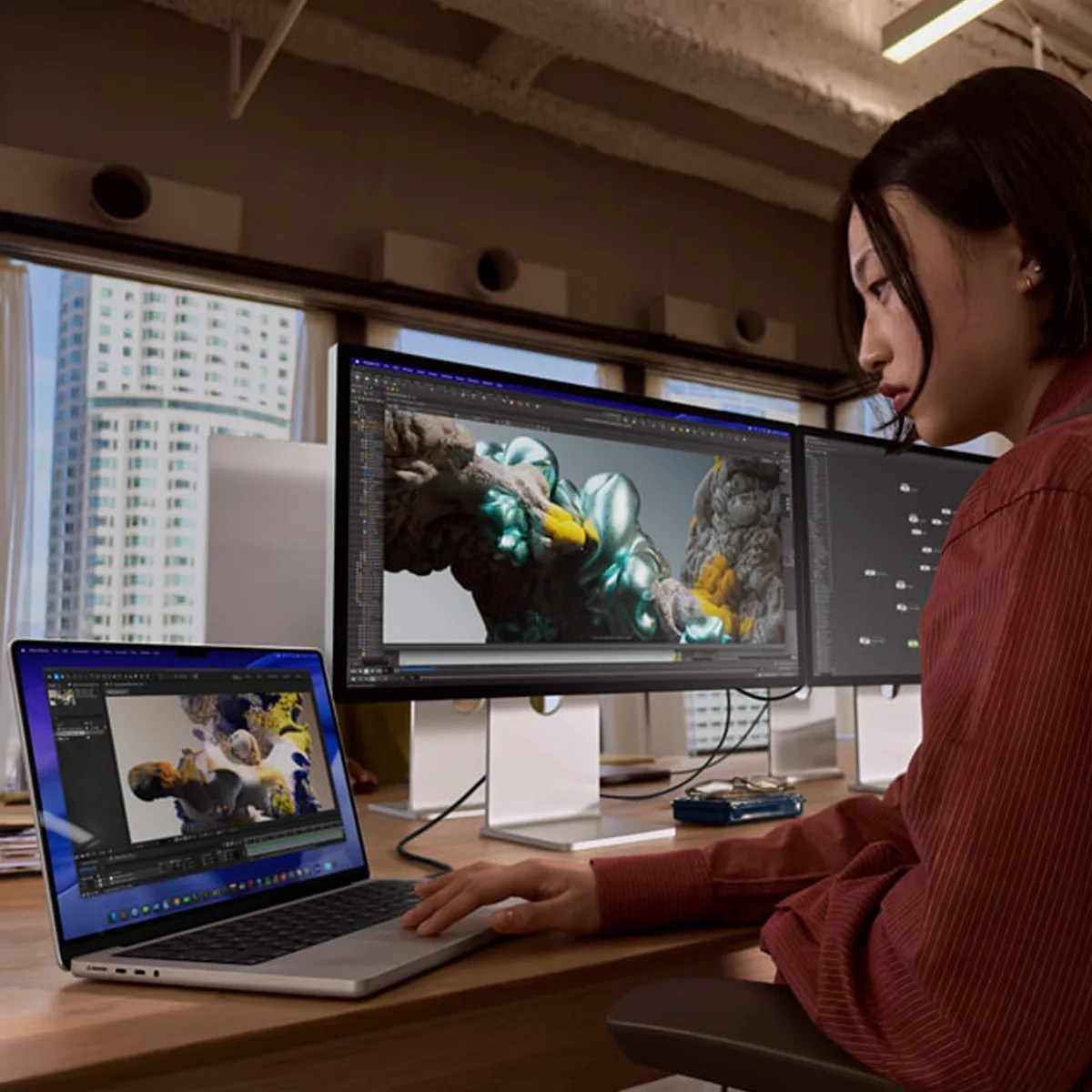 Person working on 3D digital art displayed on a laptop and dual monitors in an office setting.