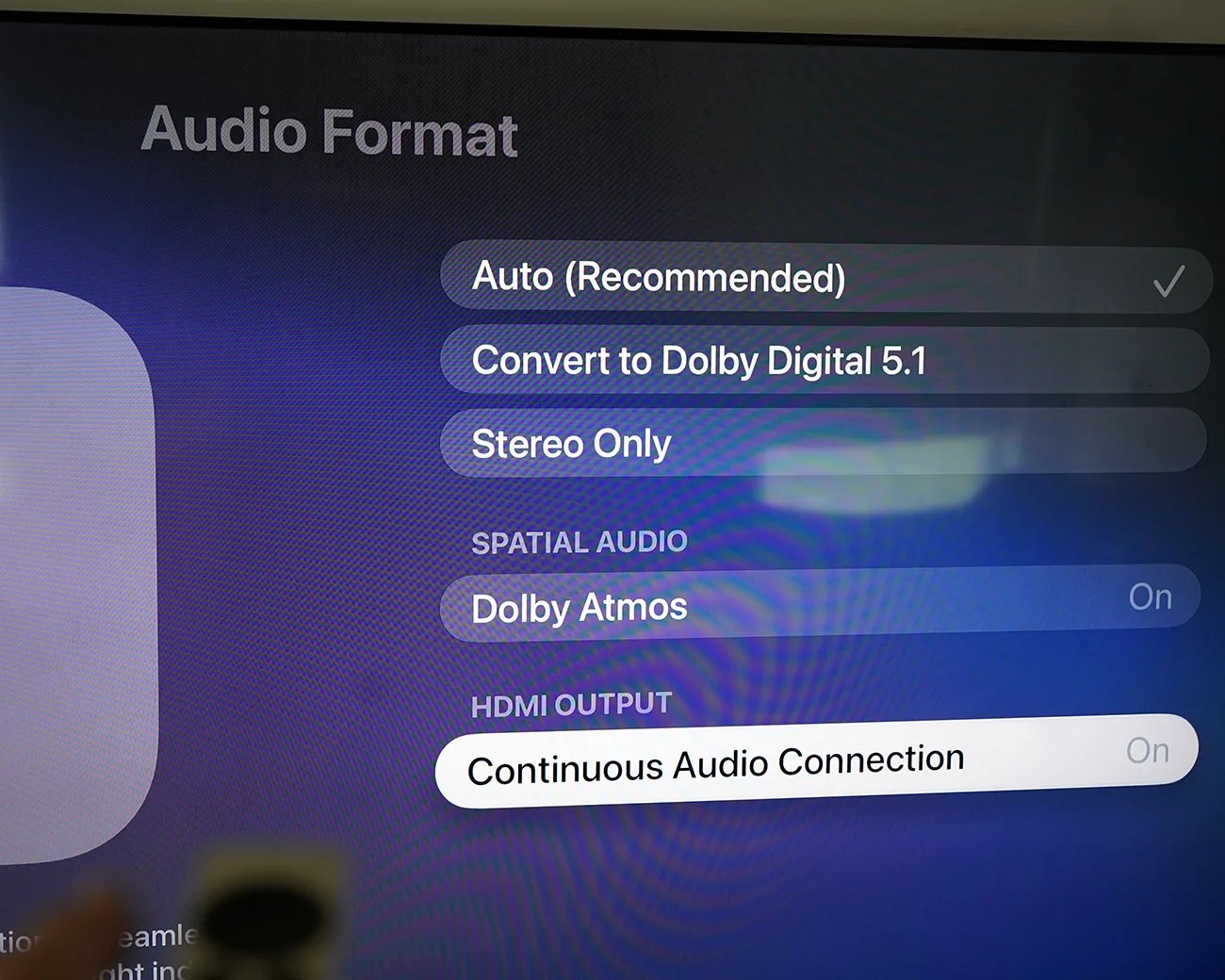 TV screen showing audio format settings with options Auto (Recommended), Convert to Dolby Digital 5.1, Stereo Only, Dolby Atmos On, and Continuous Audio Connection On.
