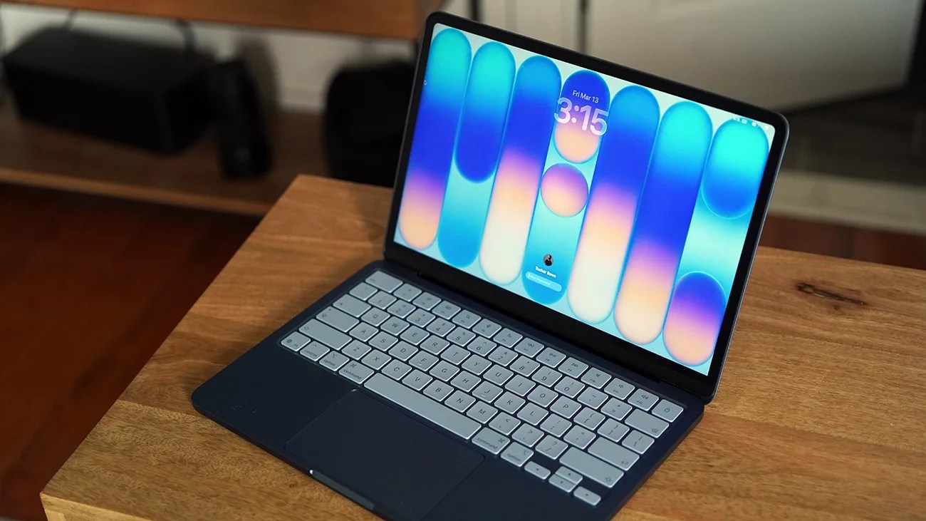 Dark blue laptop with silver keyboard and colorful abstract wallpaper on screen, placed on a wooden table.